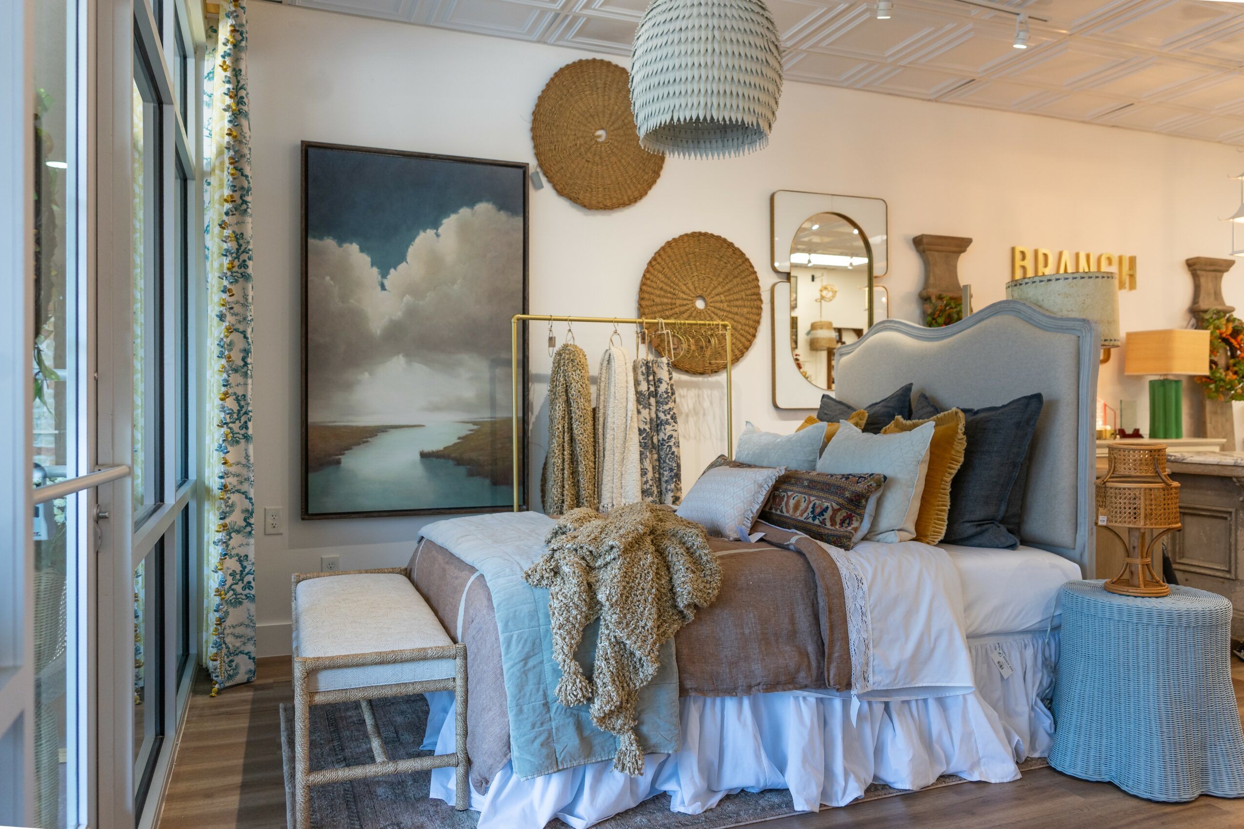 Bedroom with bed, pillows, blanket, wall decor, and window with curtains, in a cozy, well-decorated space.