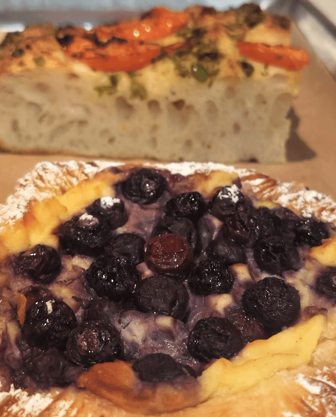 Slice of blueberry pie with crust and blueberries on top, dusted with powdered sugar.