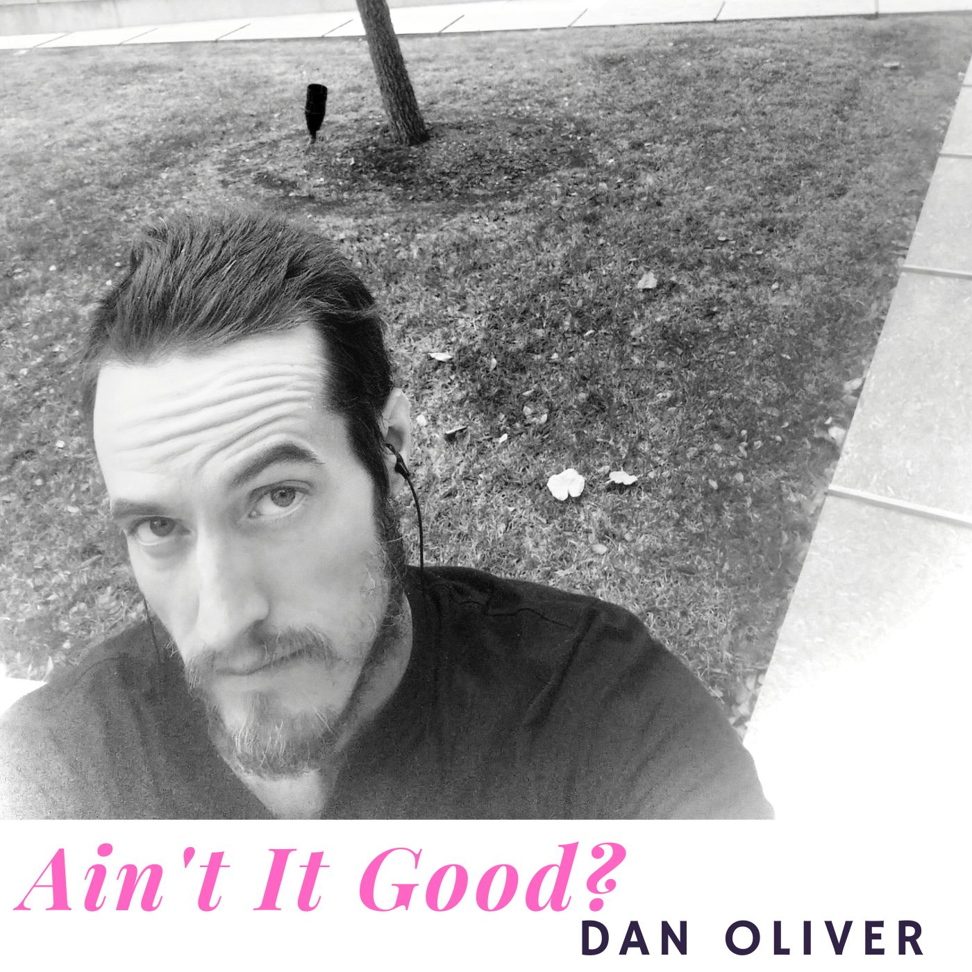 Black and white selfie of a man with dark hair and beard outdoors near a tree and sidewalk.