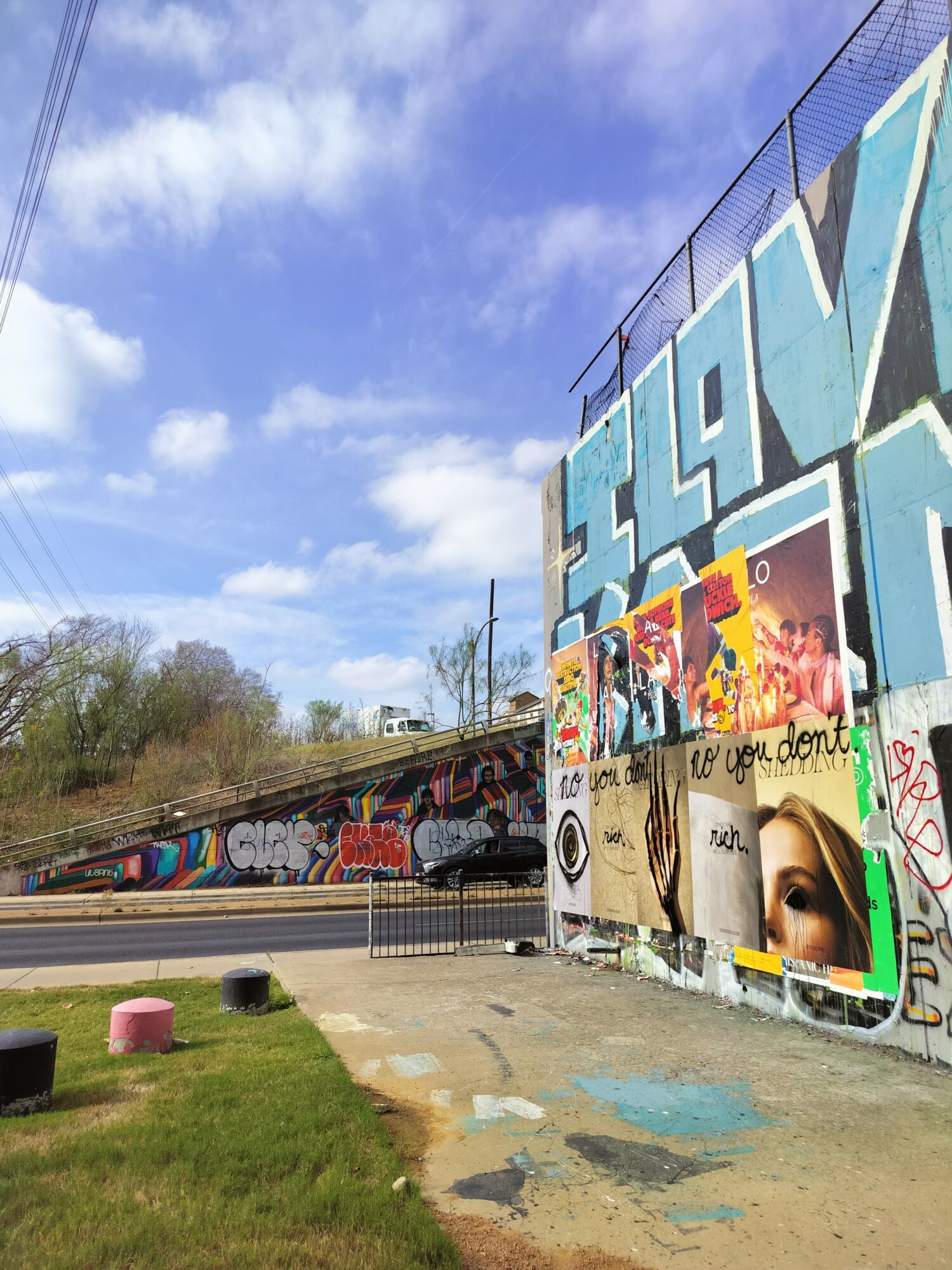 Graffiti-covered wall with colorful artwork, a train passing by, and a partly cloudy sky above.