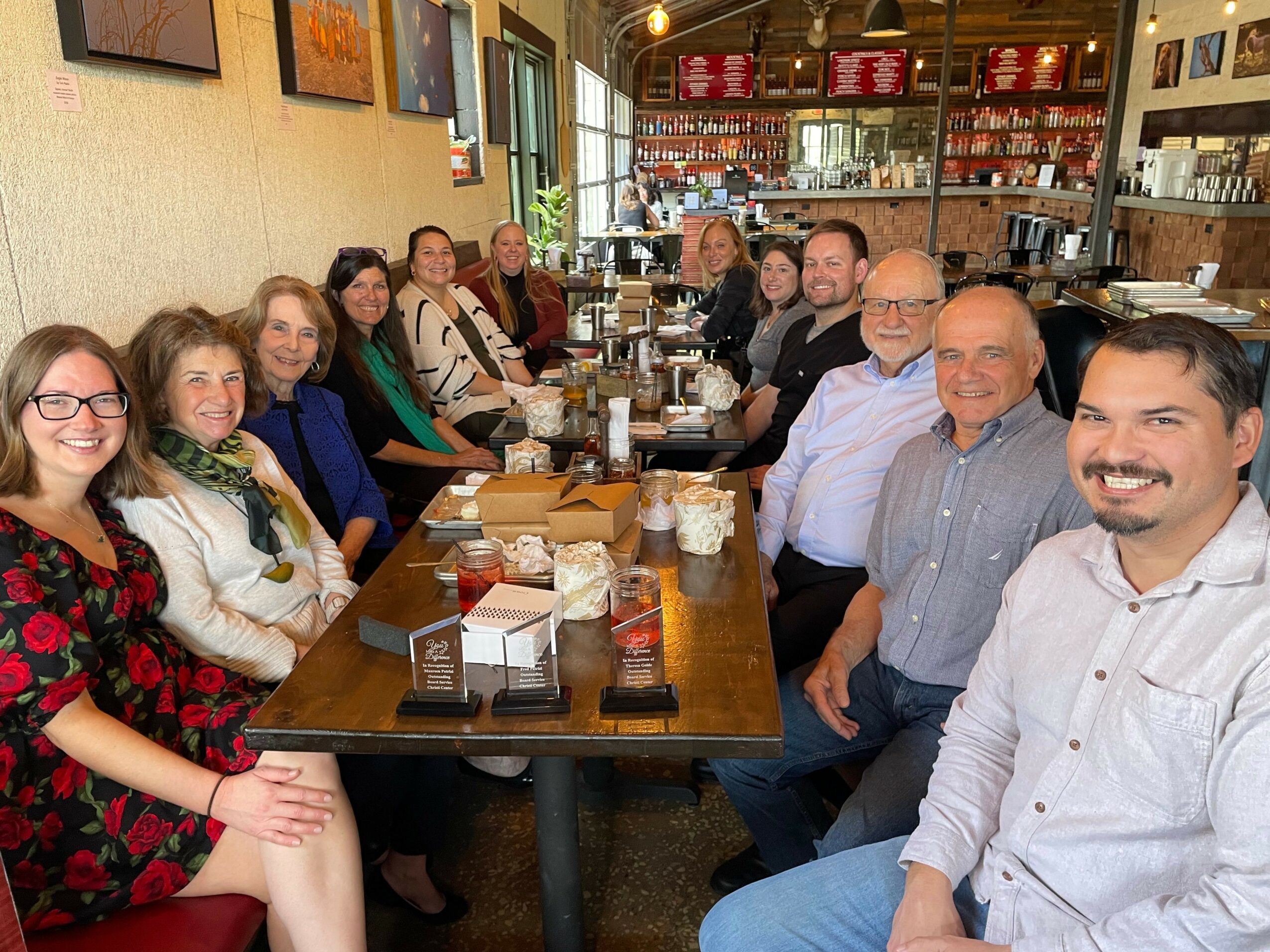 Group of people sitting around a long table in a restaurant, smiling and enjoying a meal.