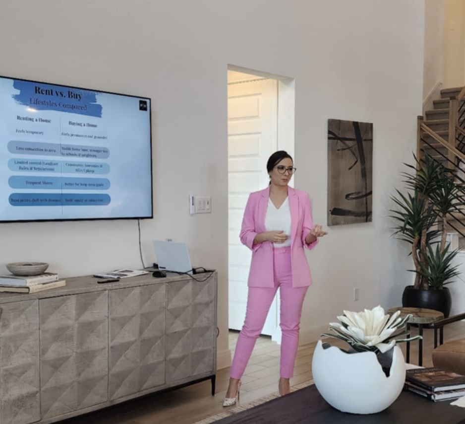 Woman in pink suit standing in a modern room, holding a phone, near a large plant and a wall art piece.