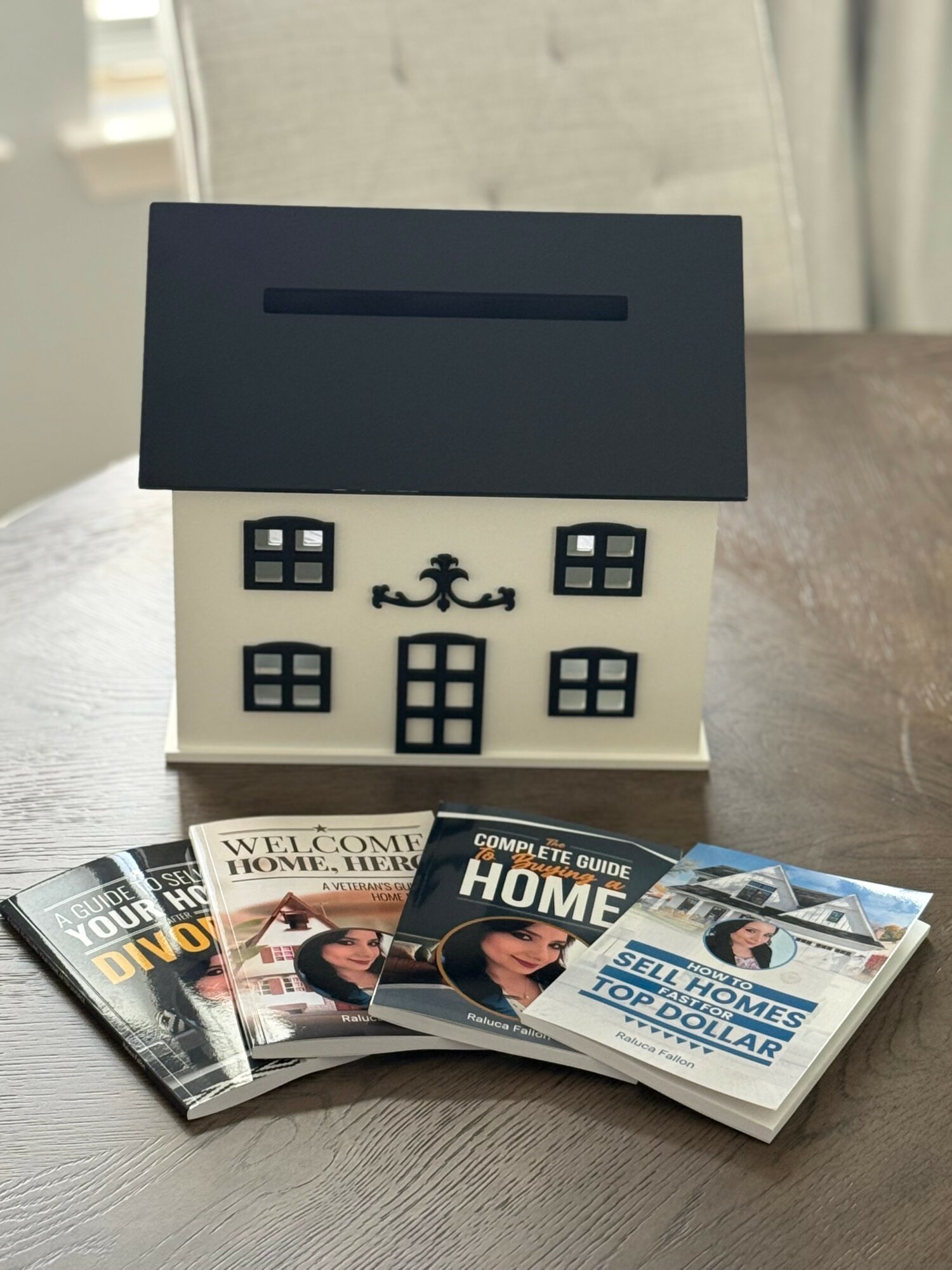 Small decorative house with black roof and windows, surrounded by real estate magazines on a wooden surface.