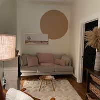Living room with a beige sofa, round wall art, and a small wooden coffee table, with a sliding door to the right.
