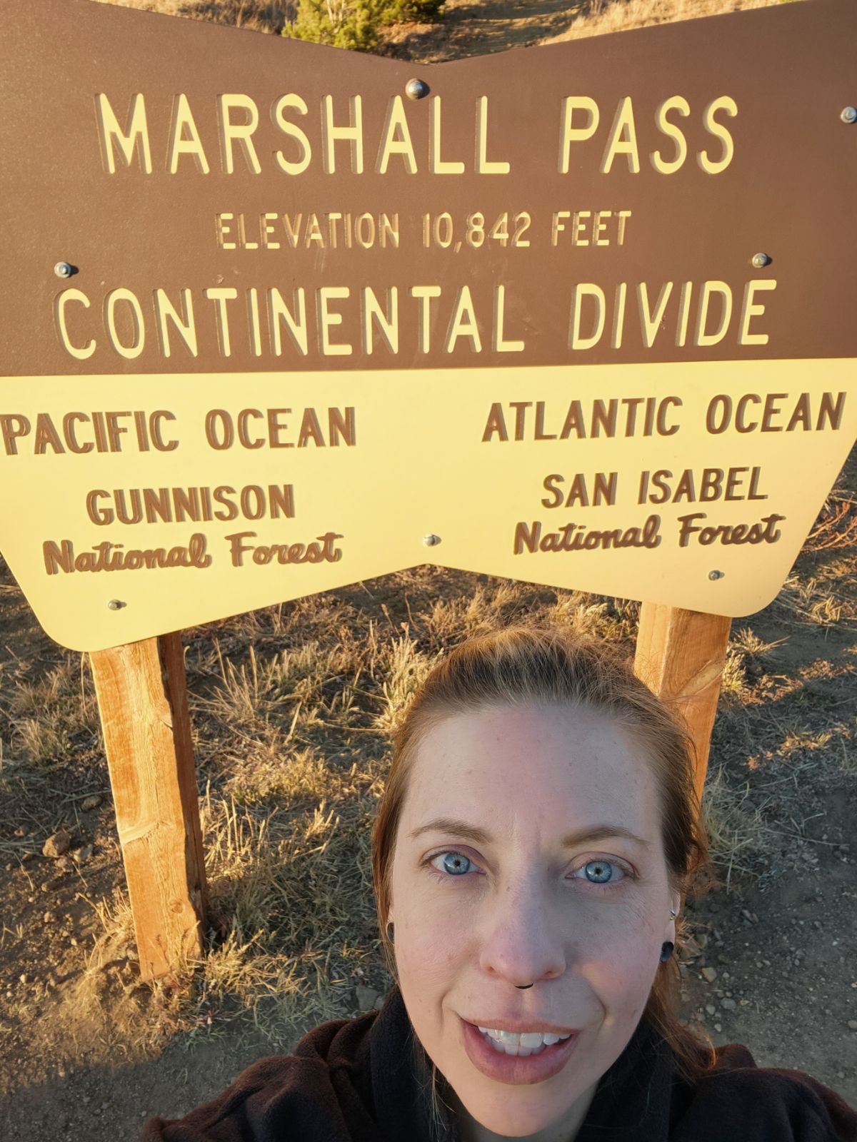 Young woman with blue eyes and brown hair taking a selfie outdoors near a sign at Marshall Pass.