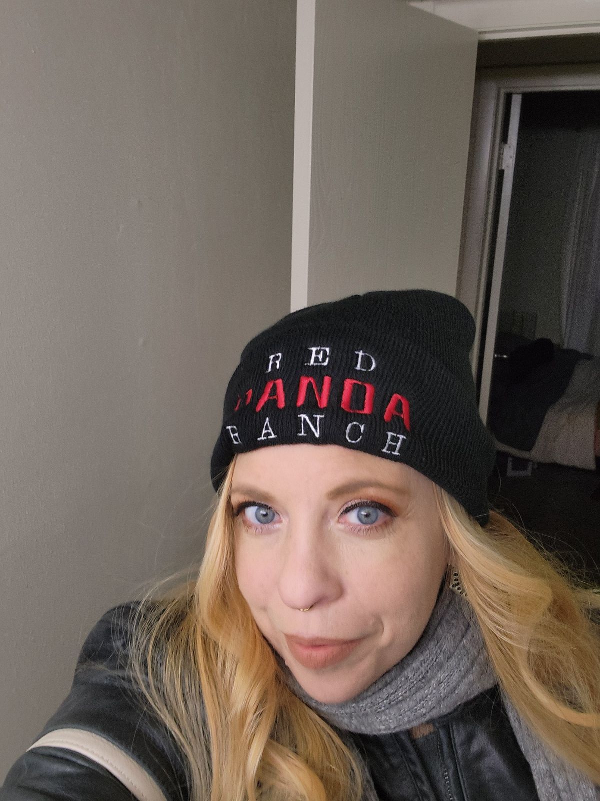 Woman with blonde hair wearing a black beanie and gray scarf indoors.