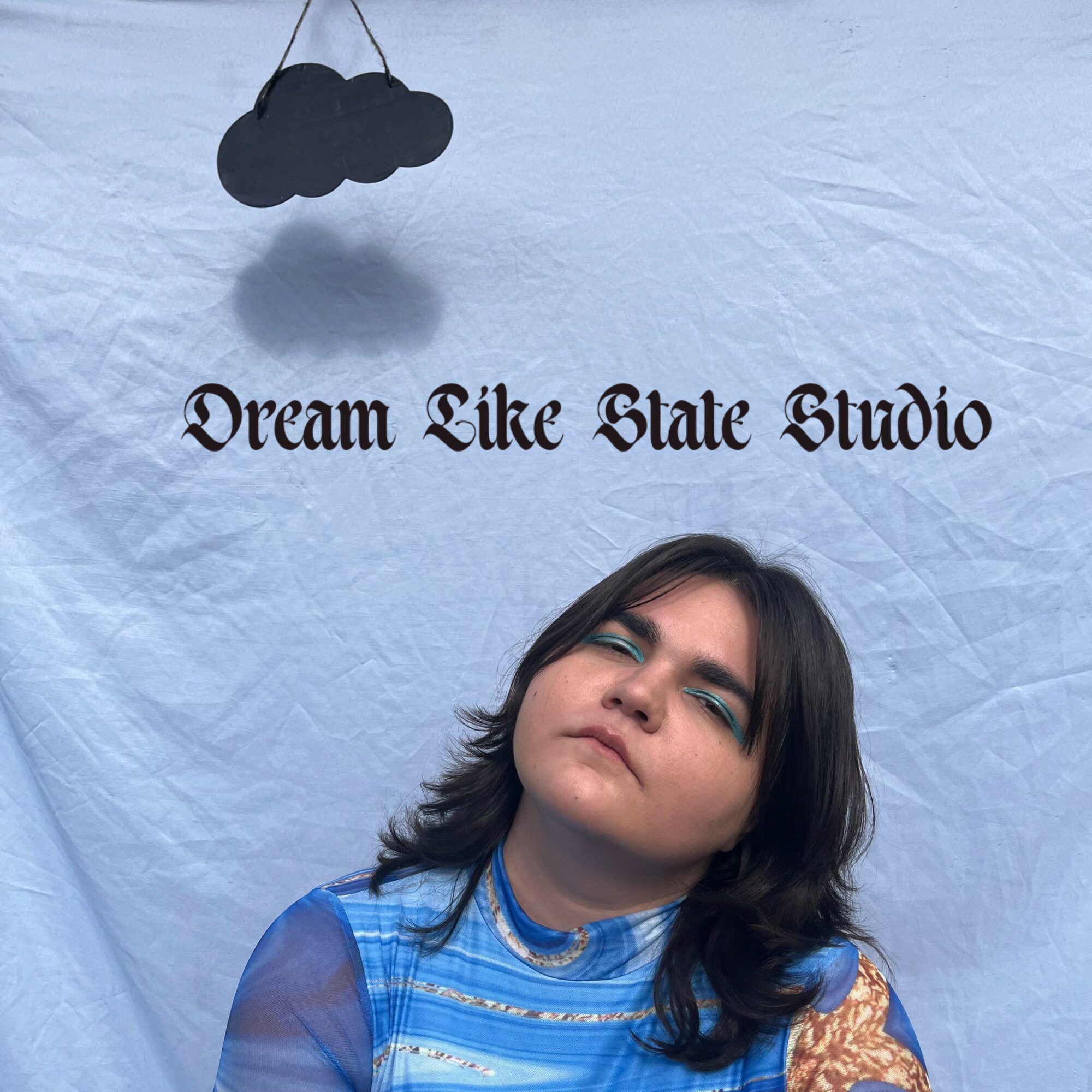 Young woman with dark hair and blue eyeshadow, posing against a light background with text and a cloud decoration.