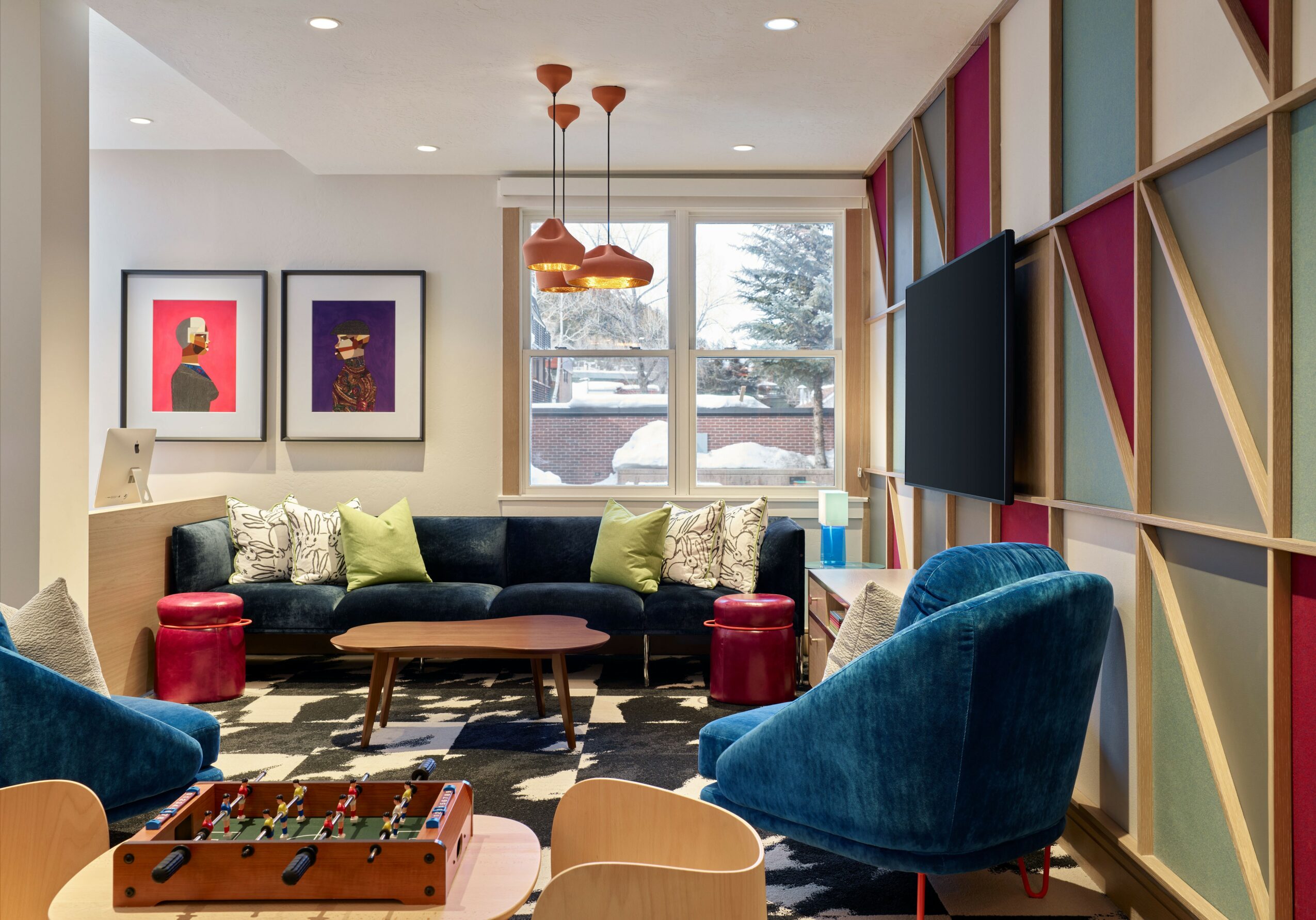 Living room with colorful geometric wall, blue chairs, black sofa, window with snow outside, and wall art.