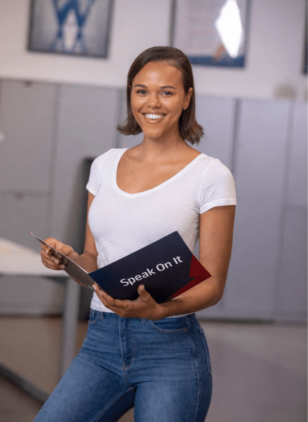 Smiling woman holding a tablet and a folder in an office setting.