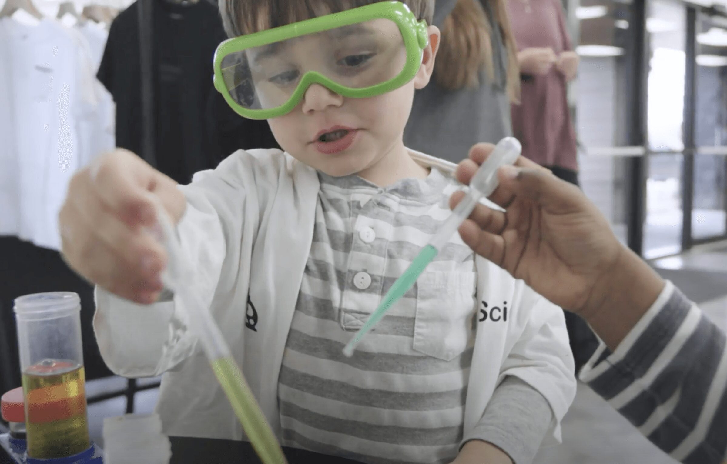 Child wearing safety goggles conducts a science experiment with a dropper and test tube.