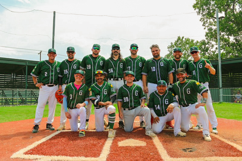 Group of baseball players in green uniforms posing on a baseball field.