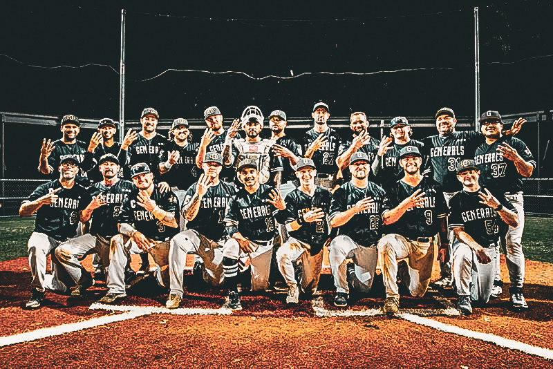 Group of baseball players in black uniforms posing on a baseball field at night.