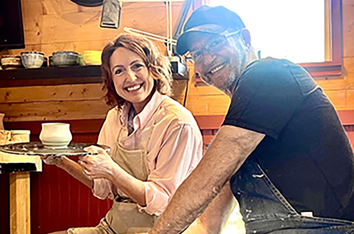 Two people smiling, one holding a tray, in a wooden interior setting.