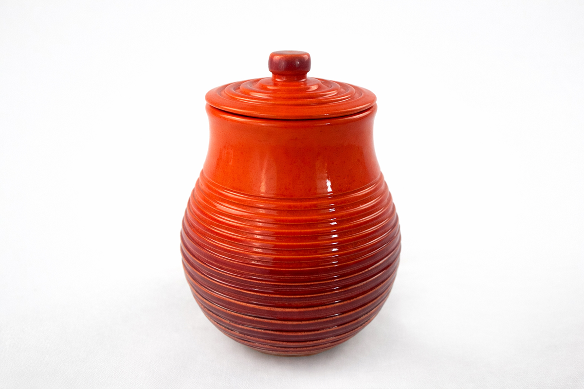 Red ceramic jar with a lid and horizontal ridges, set against a white background.