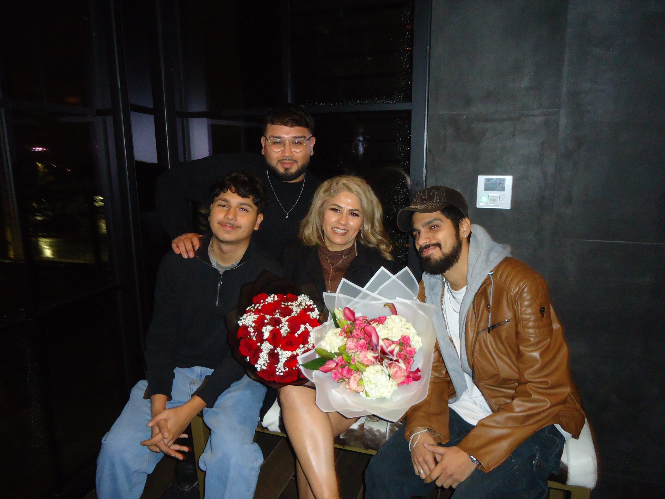 Four people sitting and standing indoors, one woman holding a bouquet of flowers, smiling.