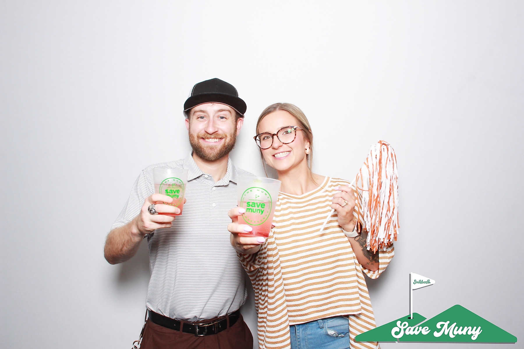 Two smiling people holding drinks and a pom-pom, standing against a plain white background.