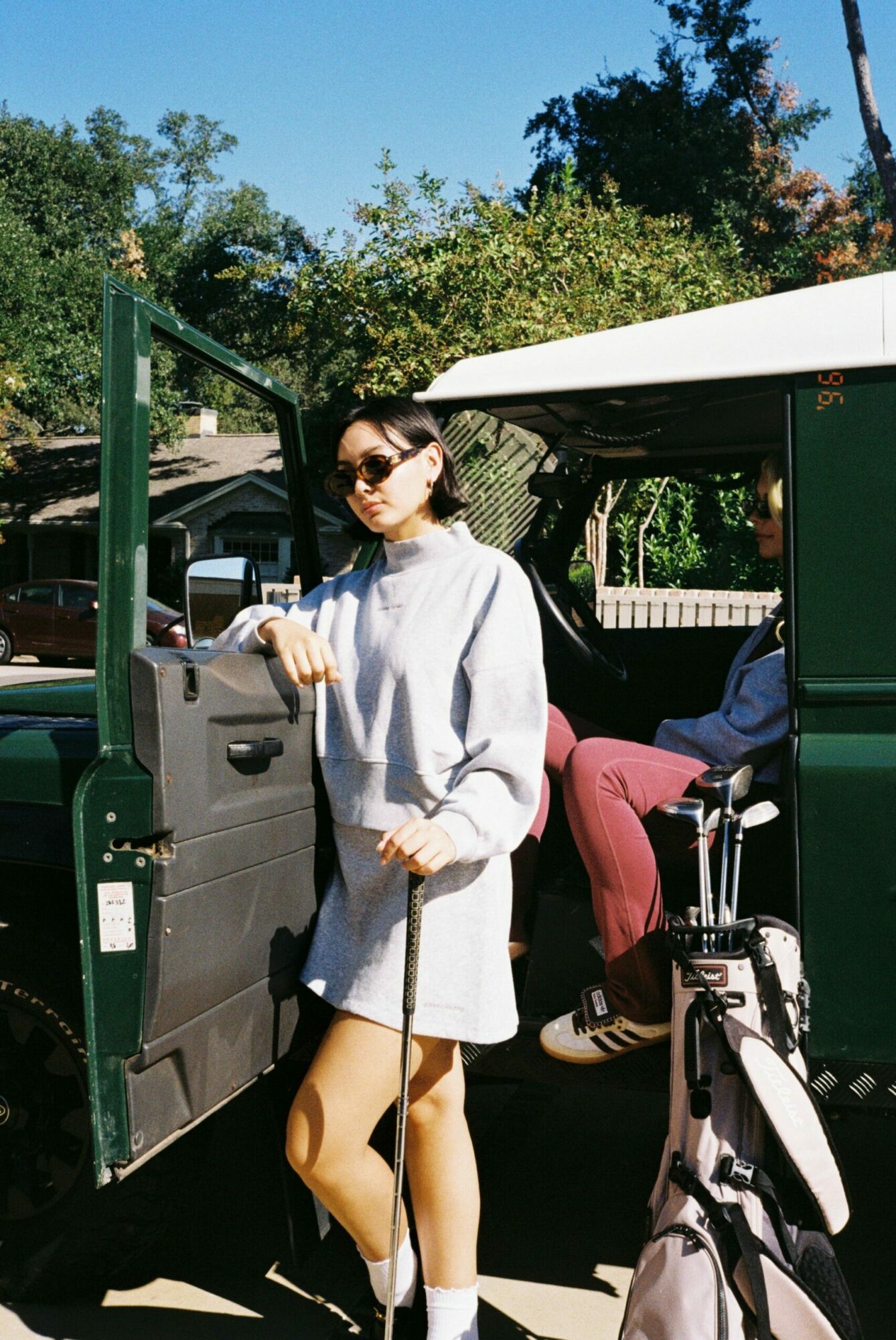 Person standing next to a green train car, holding a bag, wearing sunglasses and a gray jacket.
