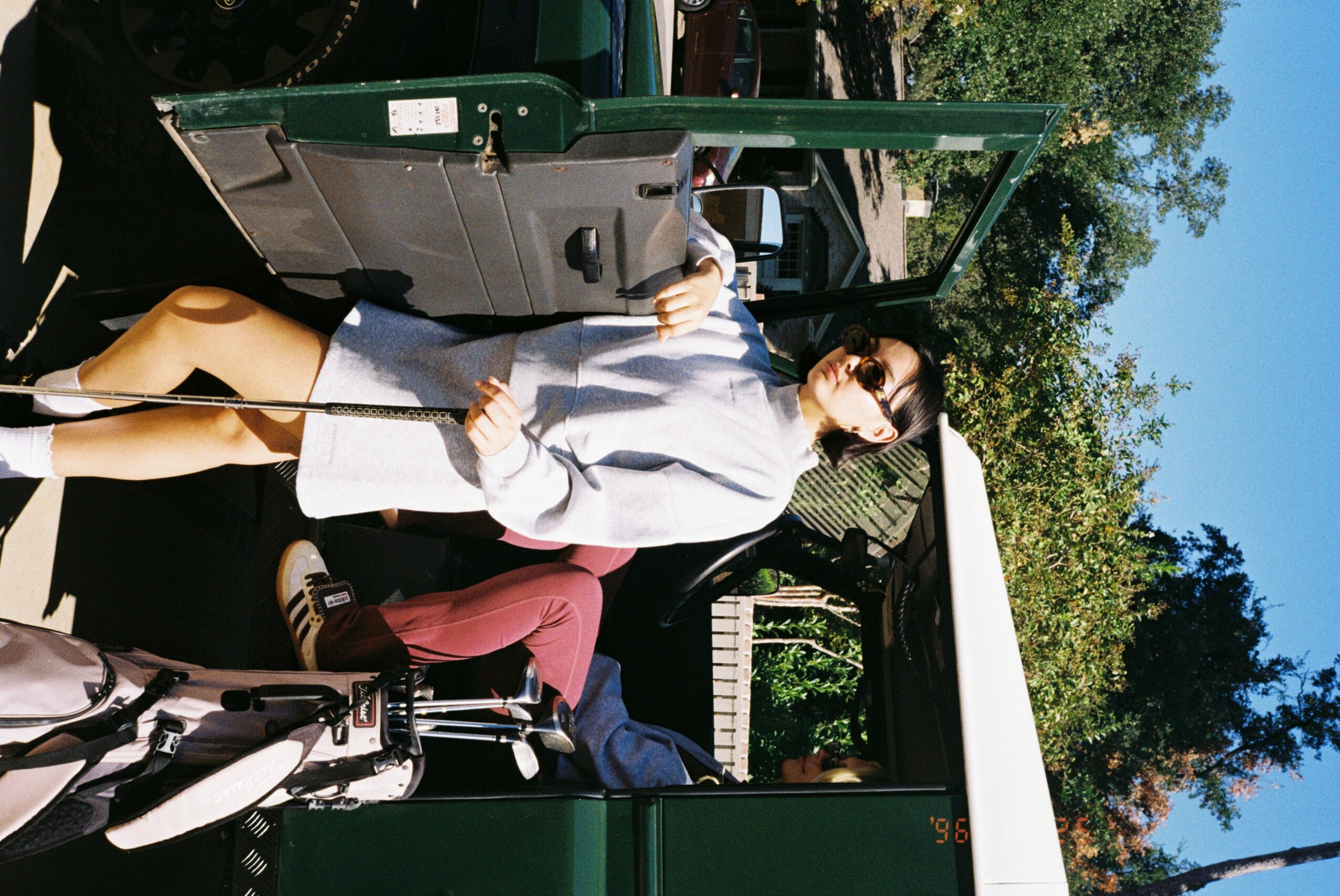Person standing next to a green train car, holding a bag, wearing sunglasses and a gray jacket.