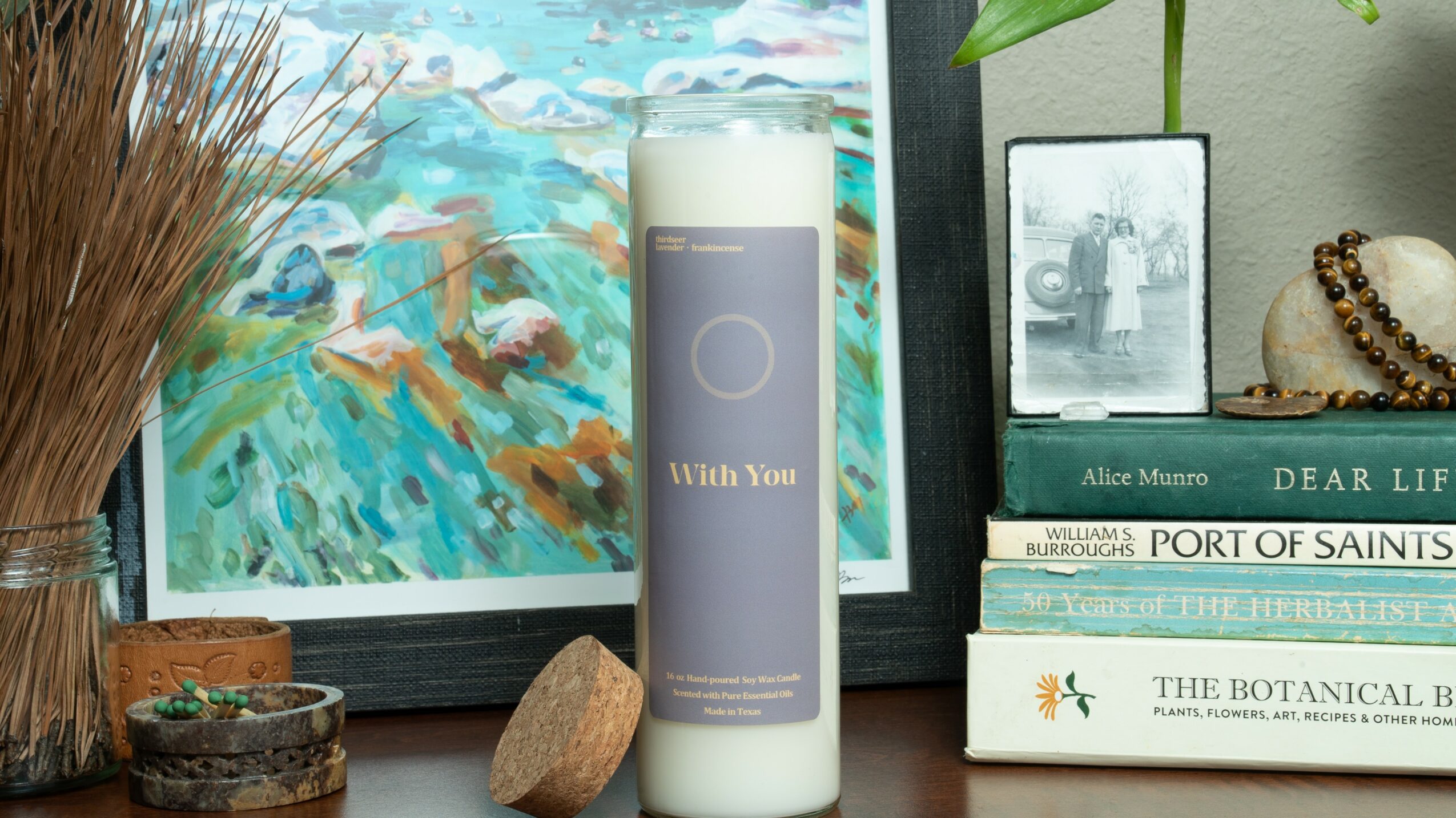 Shelf with framed painting, candle, books, and decorative items on a wooden surface.