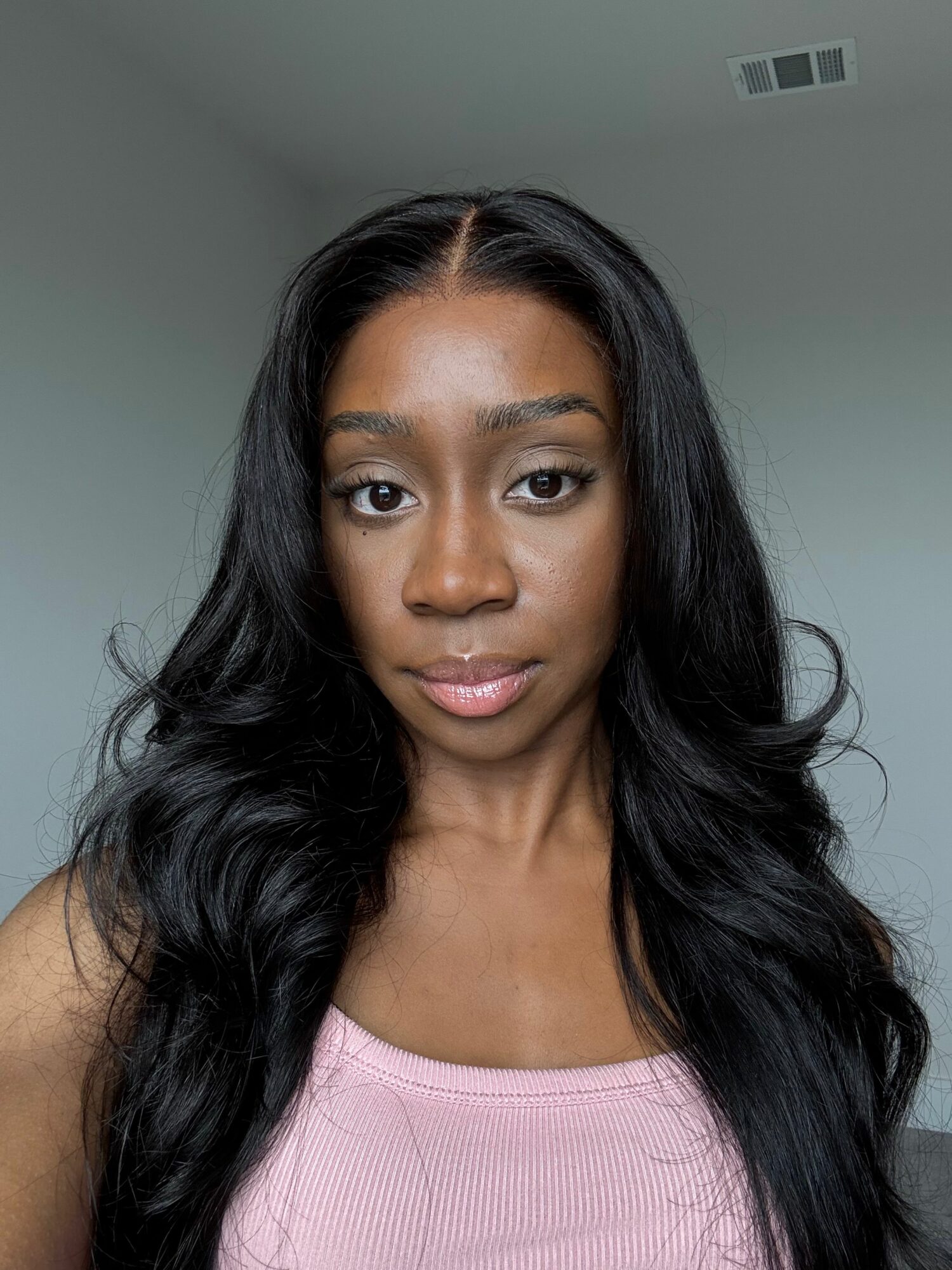 Young woman with long, wavy black hair and a pink top, looking directly at the camera.