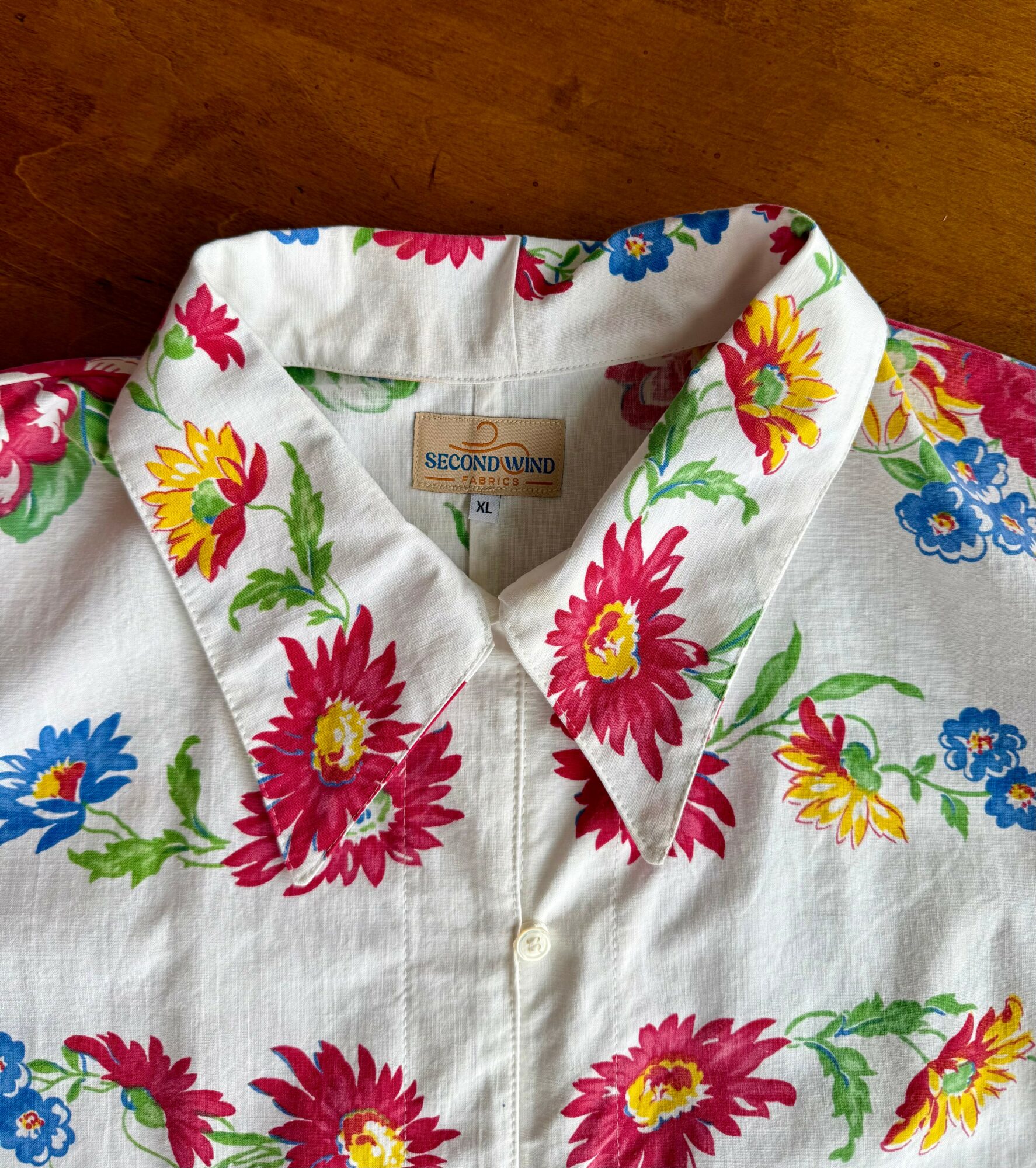 White shirt with colorful floral pattern, collar, and button front, laid flat on a wooden surface.