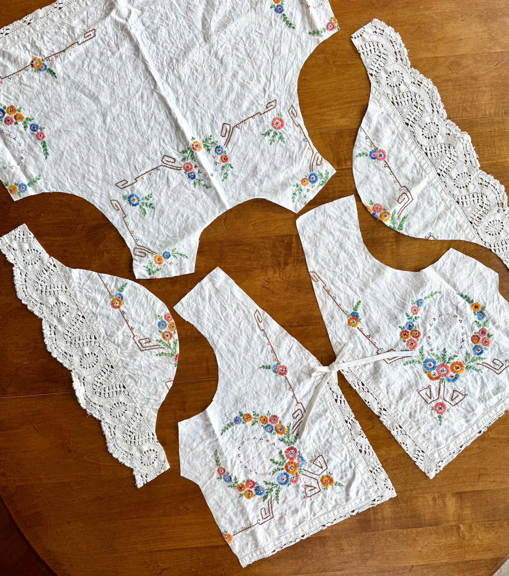 Four embroidered fabric pieces with lace edges arranged on a wooden surface.