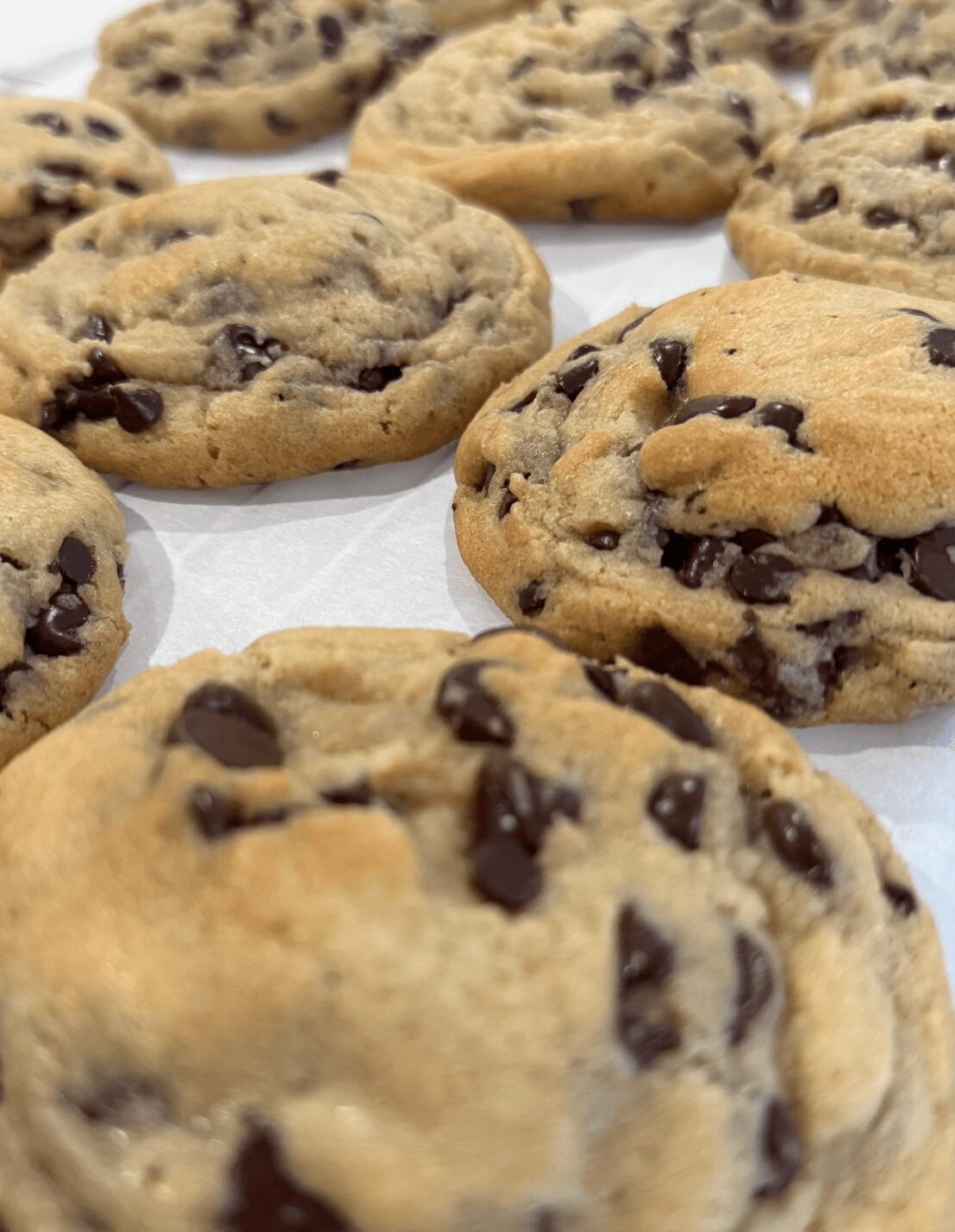 Close-up of chocolate chip cookies on a white surface, showing golden-brown edges and chocolate chips.