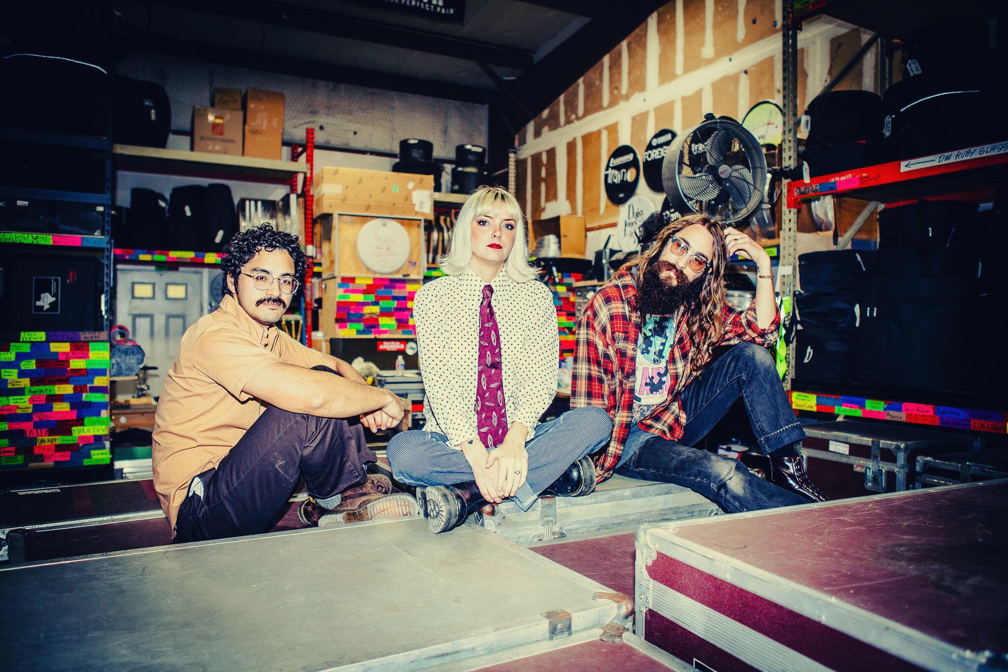 Three people sitting on the floor in a store with shelves of helmets and colorful boxes behind them.