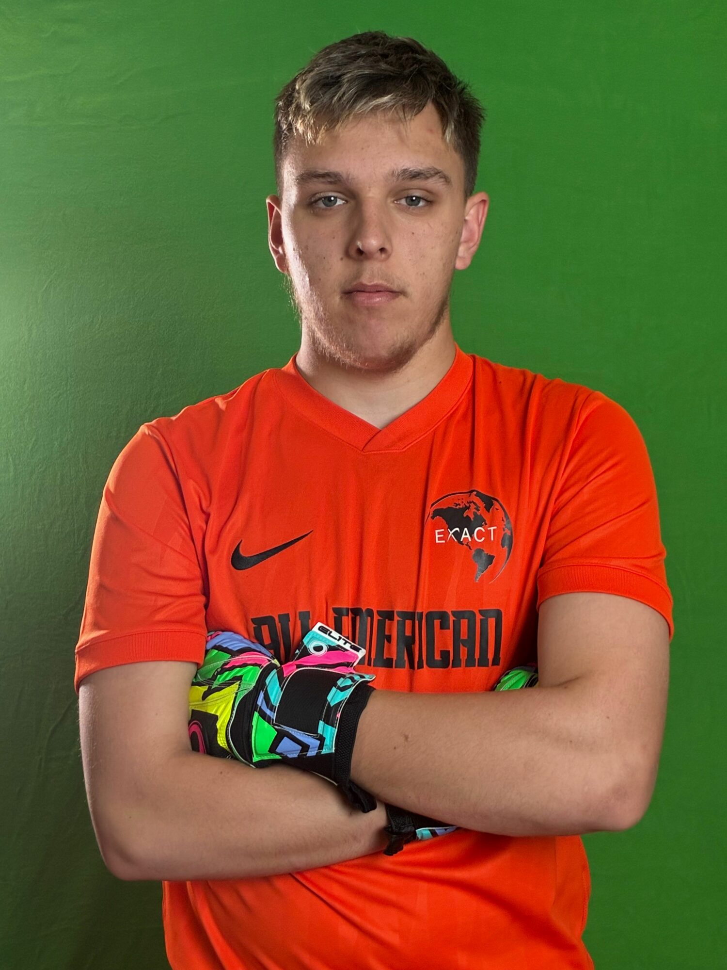 Young male athlete in orange sports jersey with arms crossed, standing against green background.