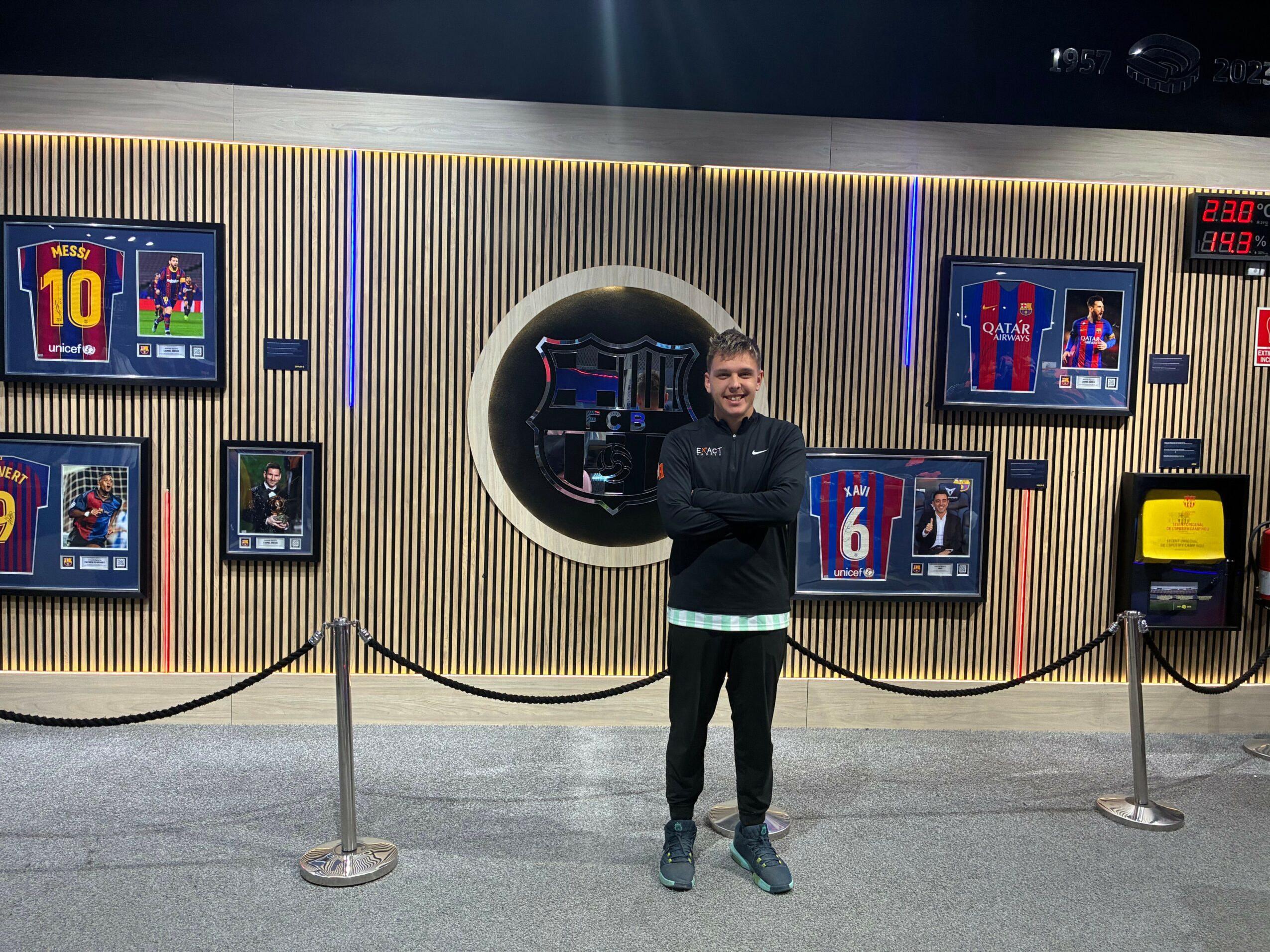 Man standing with arms crossed in front of sports-themed display with screens and a circular window.