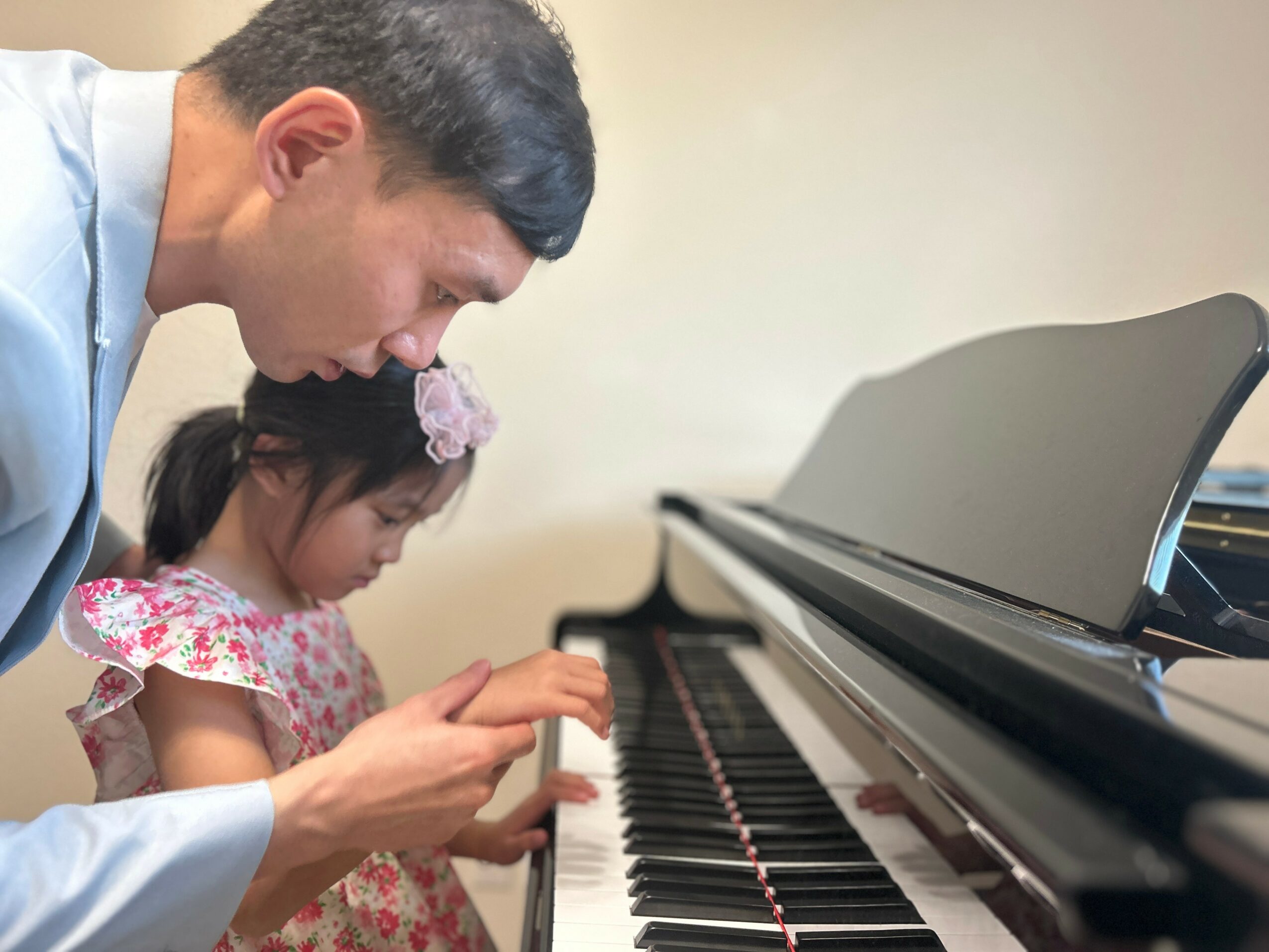 Adult and child looking at a smartphone near a piano, child playing keys, indoor setting.