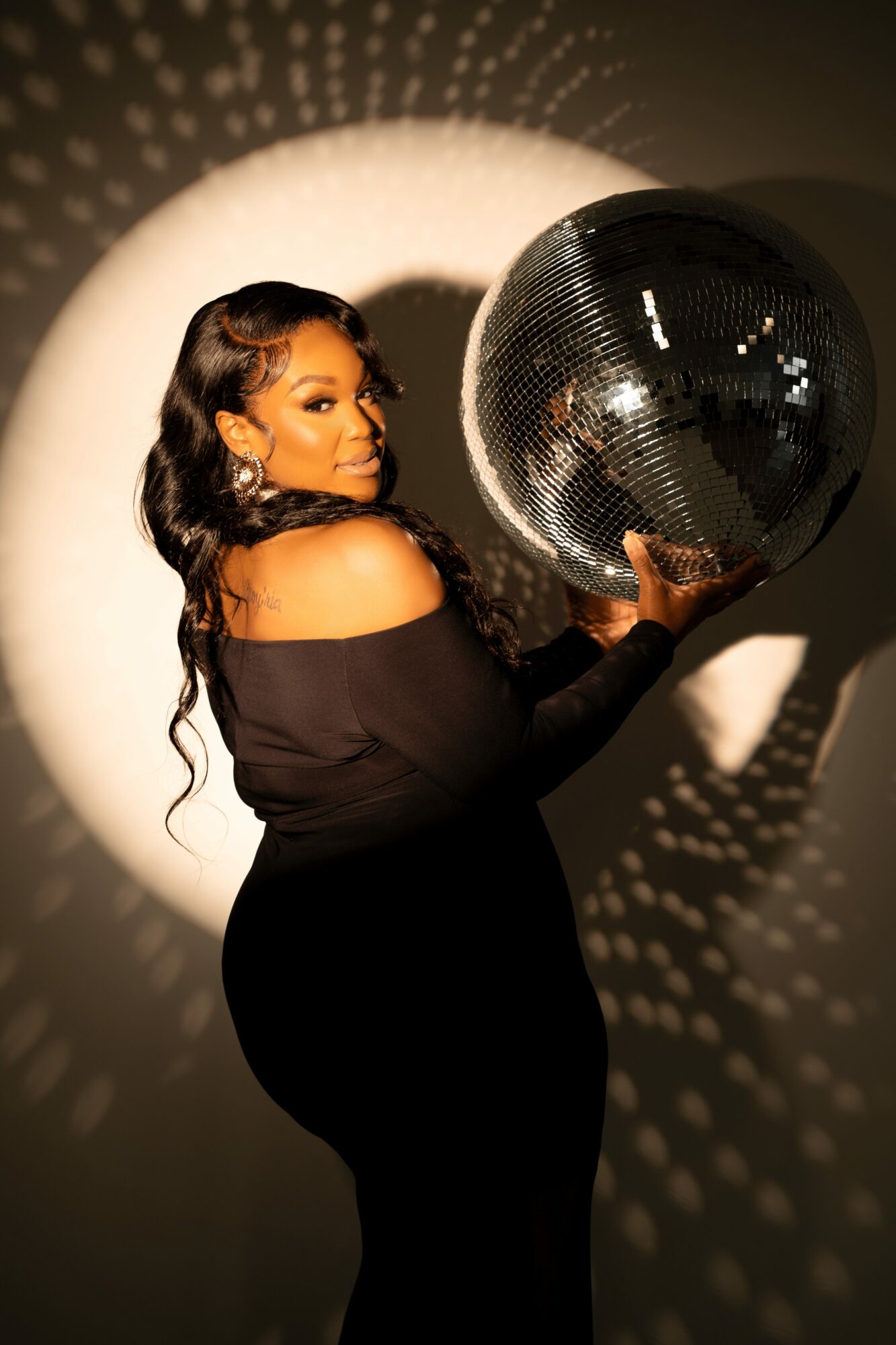 Woman holding a large disco ball with light reflections on the wall behind her.