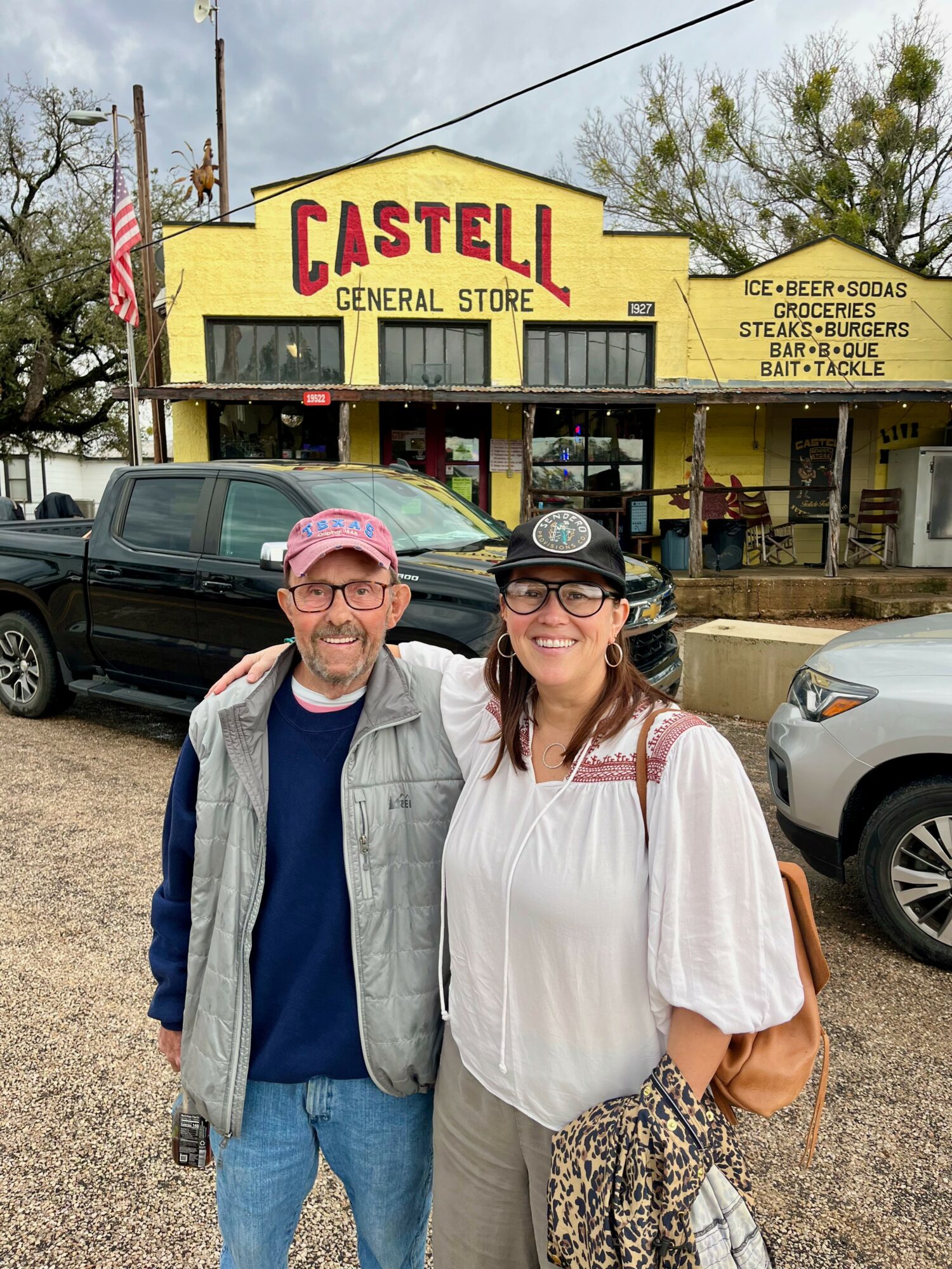Two people standing in front of a store with a yellow sign reading 'Castell General Store'.