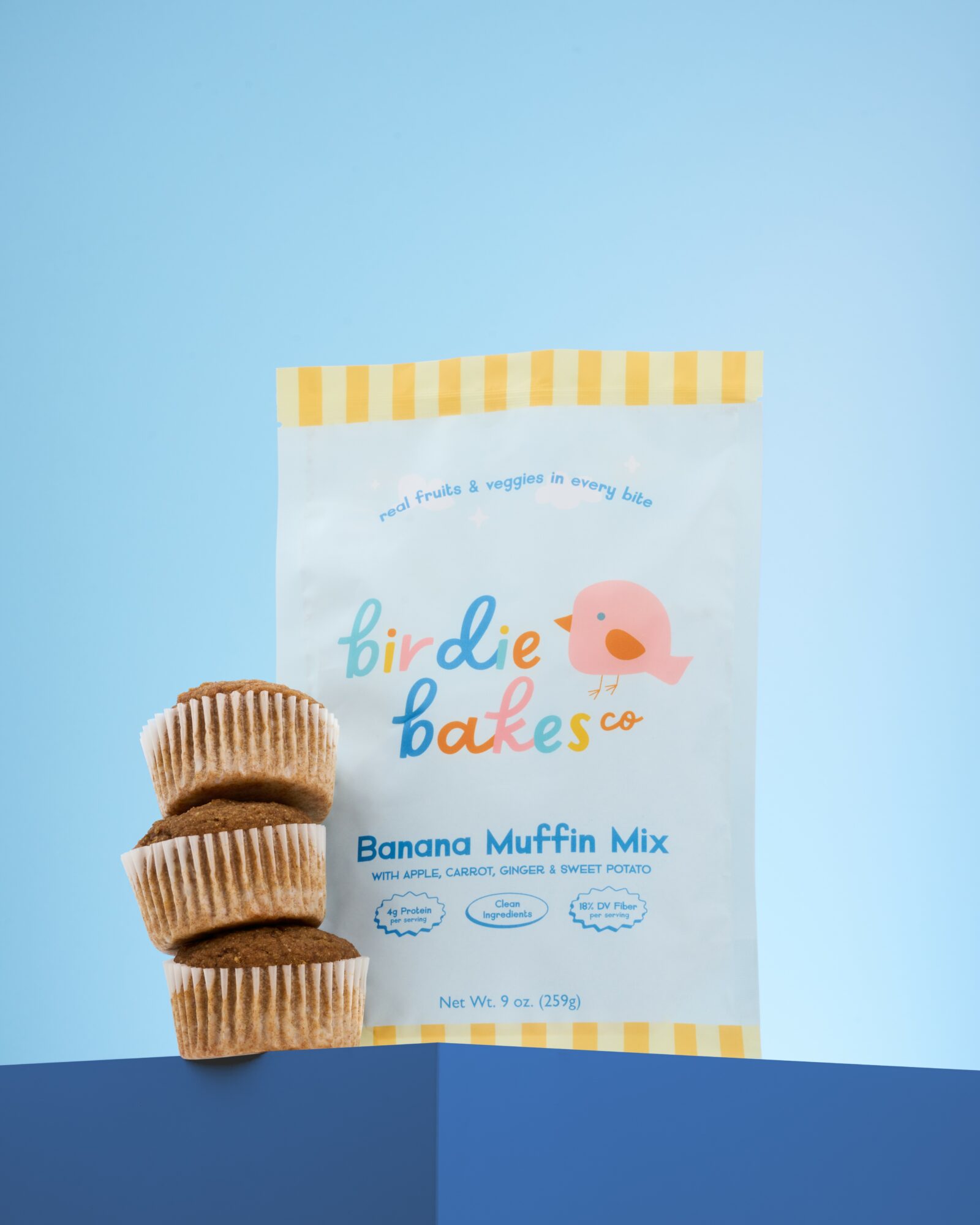 Stack of three banana muffin mix packets against a blue background with a blue surface.