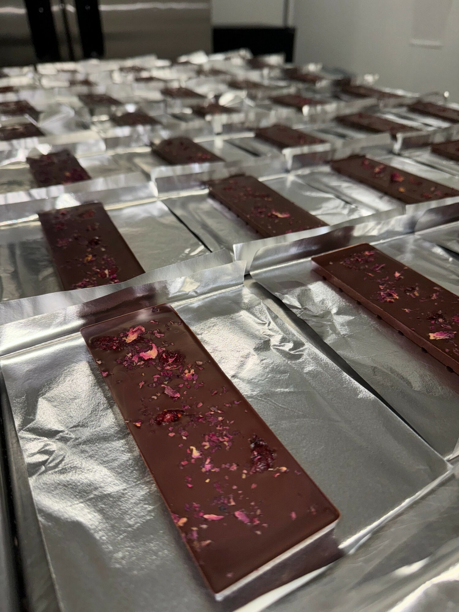 Multiple chocolate bars with pink toppings on aluminum foil, arranged on a table in rows.