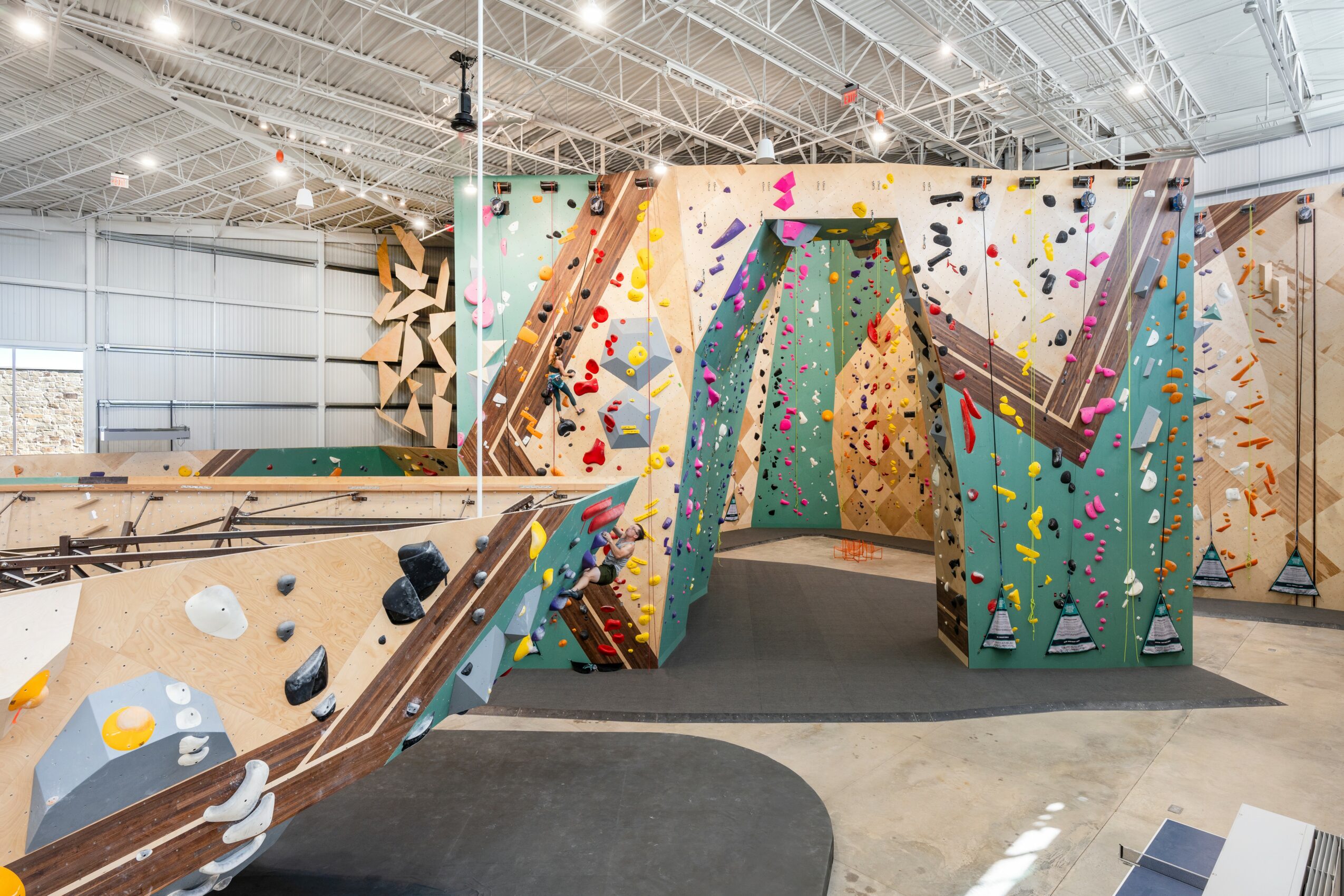 Indoor rock climbing gym with colorful climbing walls and a high ceiling, padded flooring, and climbing holds.