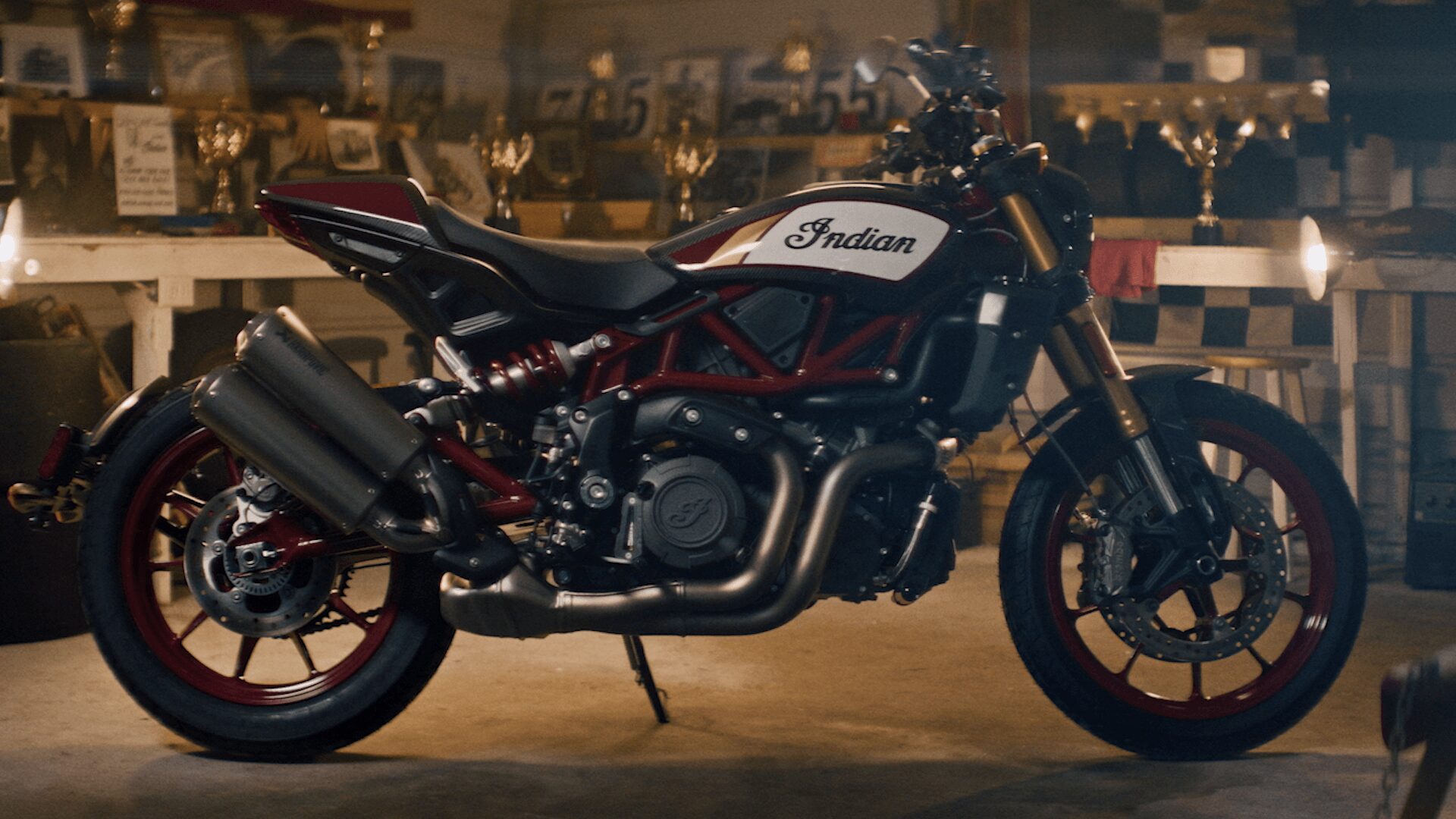 Black and white Indian motorcycle with red accents parked indoors, with trophies and shelves in the background.