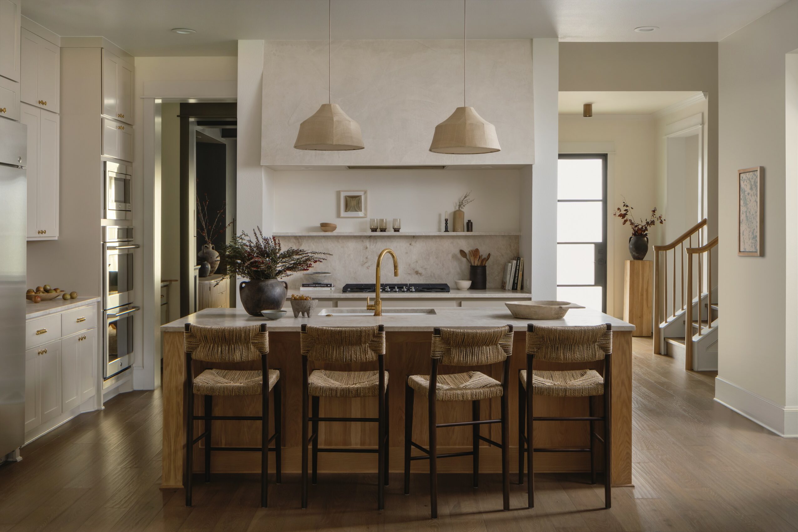 Modern kitchen with island, pendant lights, and dining area with four chairs, neutral colors, and natural light.