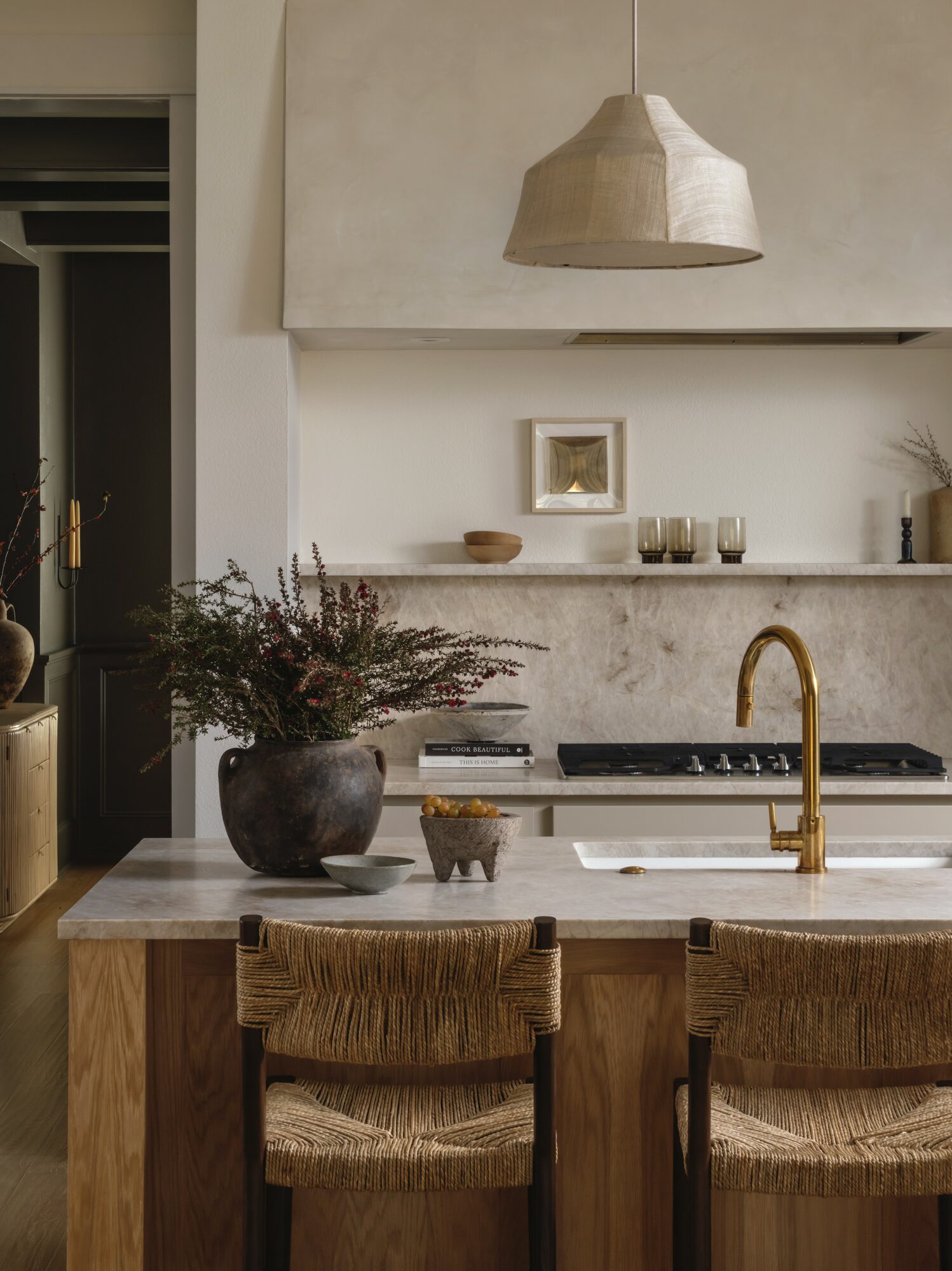 Kitchen with a marble island, gold faucet, hanging light, and decorative items on the counter.