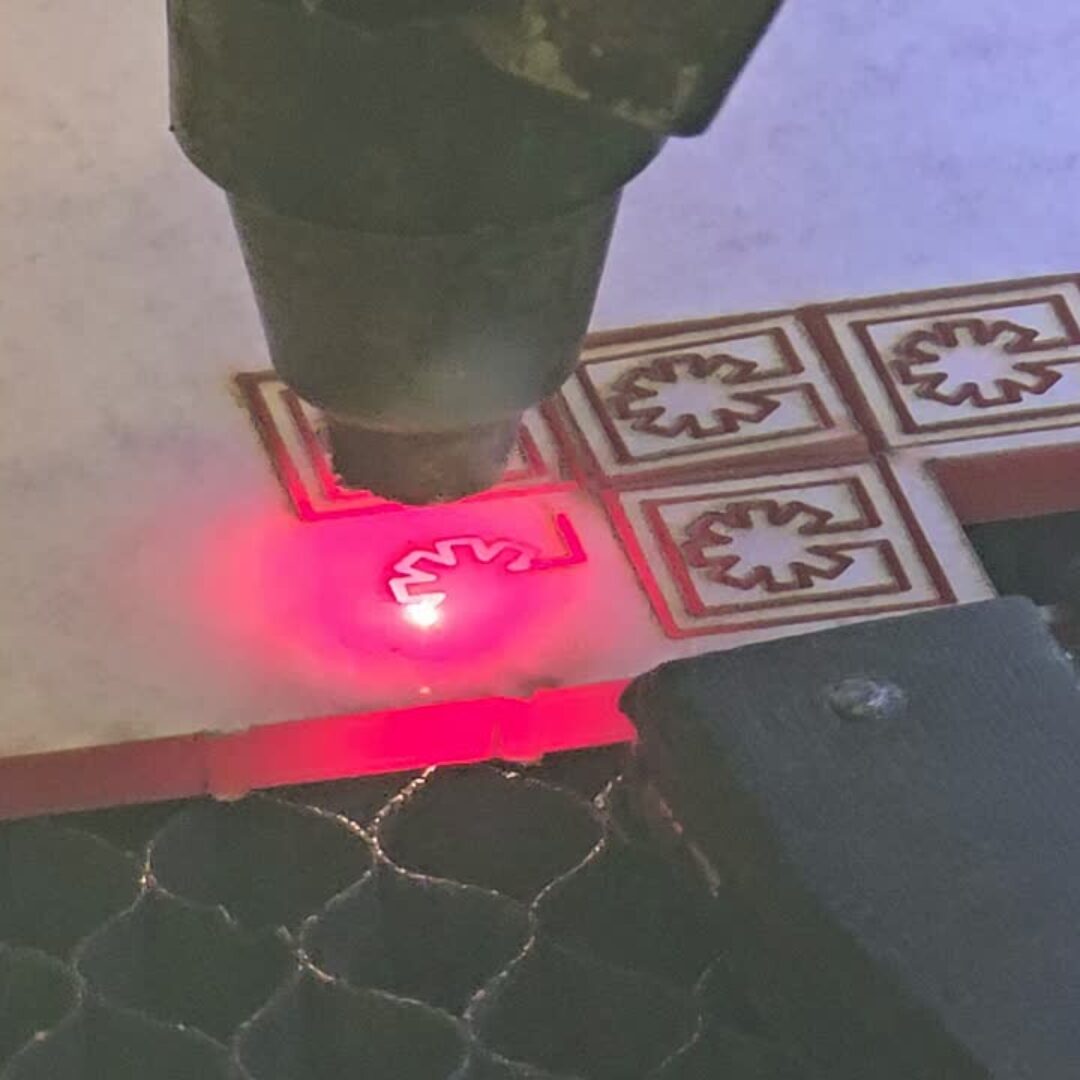 Laser cutter engraving a pattern on tiles with a red laser beam, close-up view.