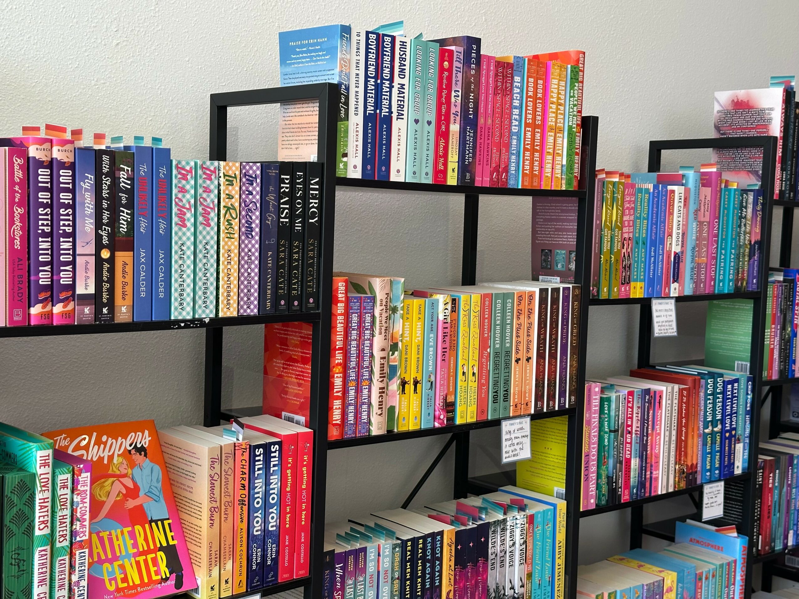 Bookshelves filled with colorful books arranged on black metal shelves against a light-colored wall.