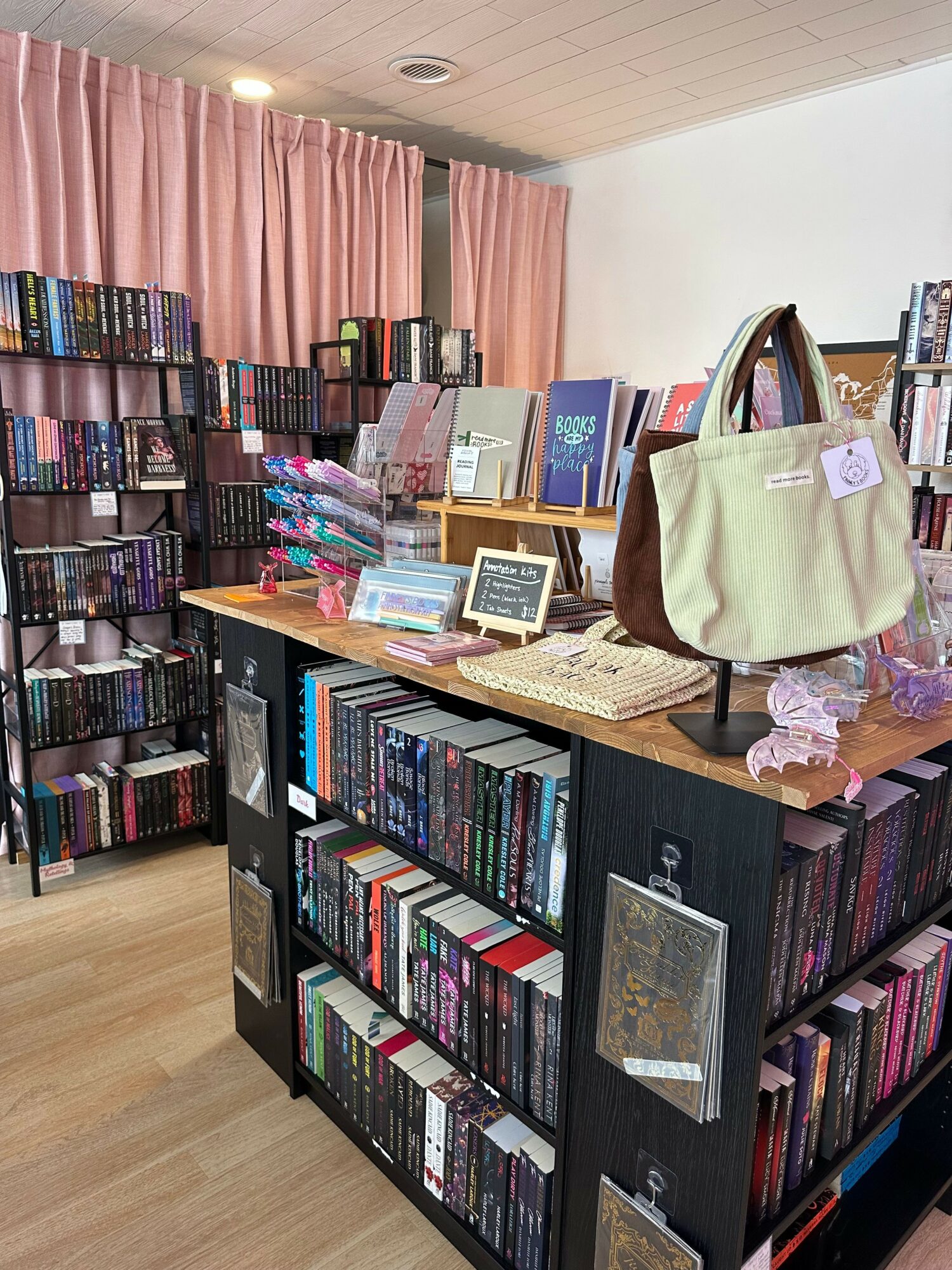 Bookshelves filled with books, a table with various items, pink curtains, and a bag on the table.