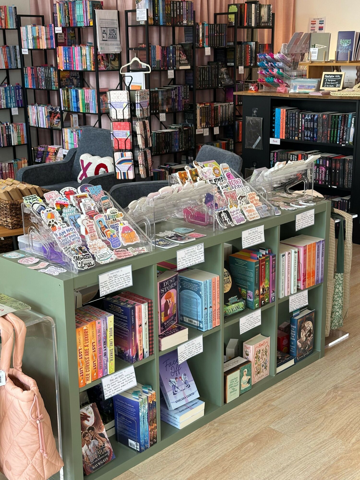Books and items displayed on a green shelf and table in a store, with shelves filled with books in the background.