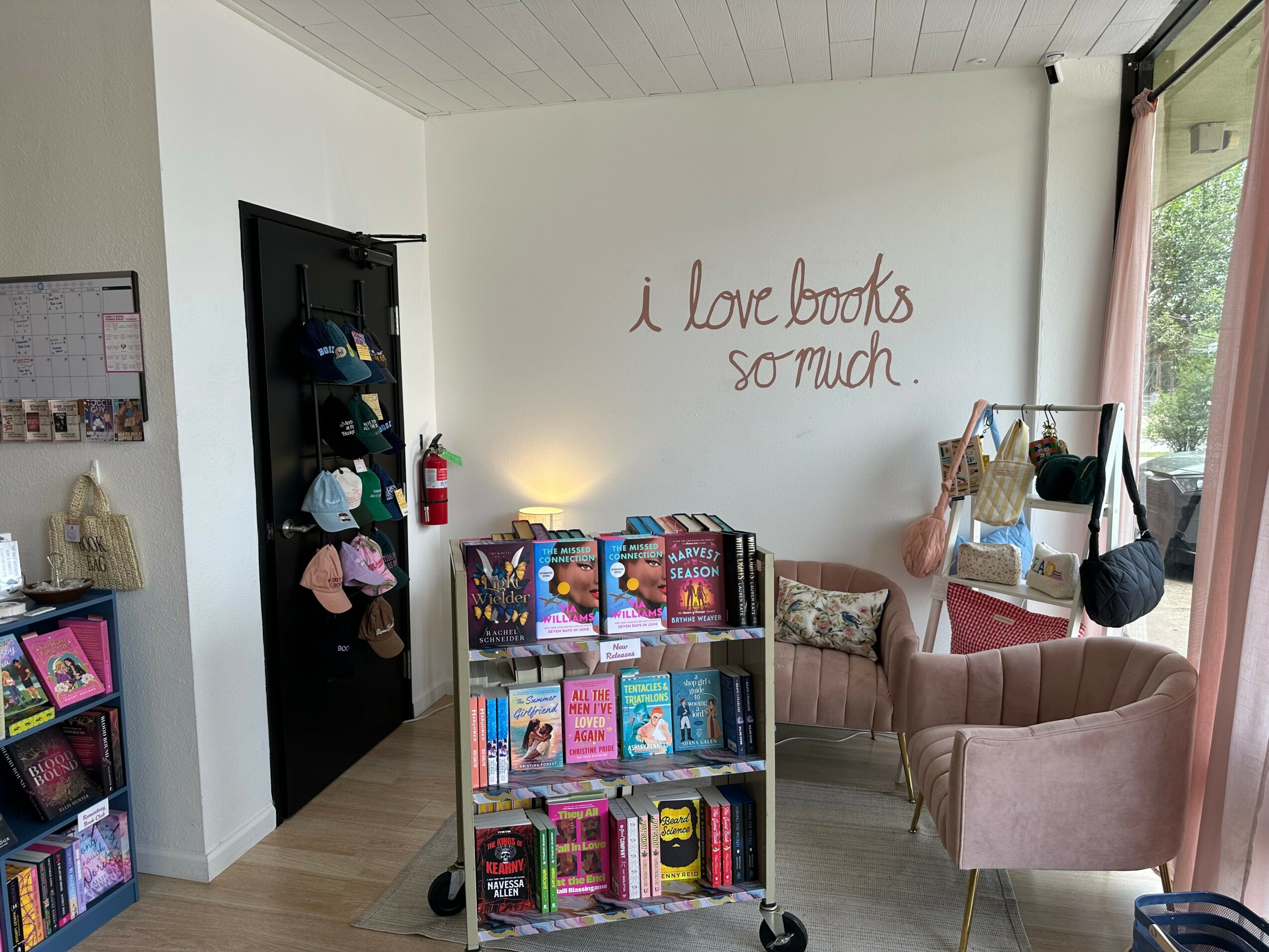 Bookshelf with books, a pink armchair, and a wall with handwritten quote, near a window with curtains.