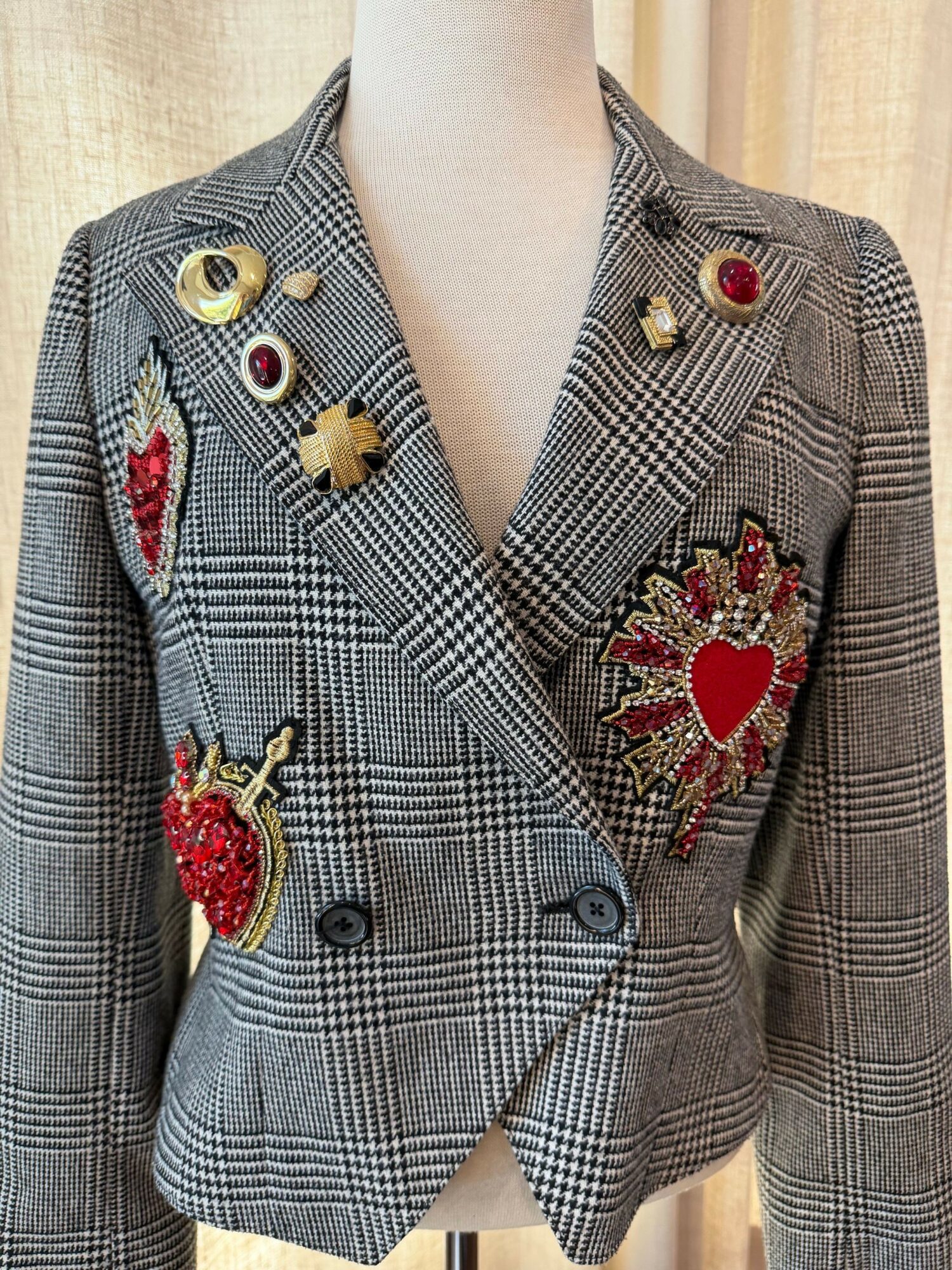 Person wearing a gray plaid blazer with embroidered patches, including a heart and a flower, and decorative buttons.