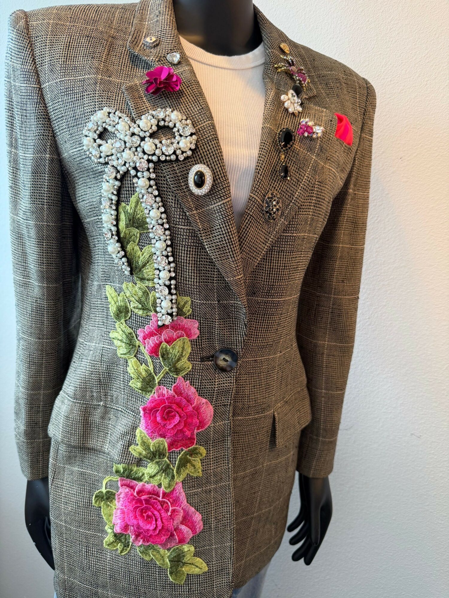 Mannequin in a brown plaid suit with floral embroidery, lying sideways on a white surface.