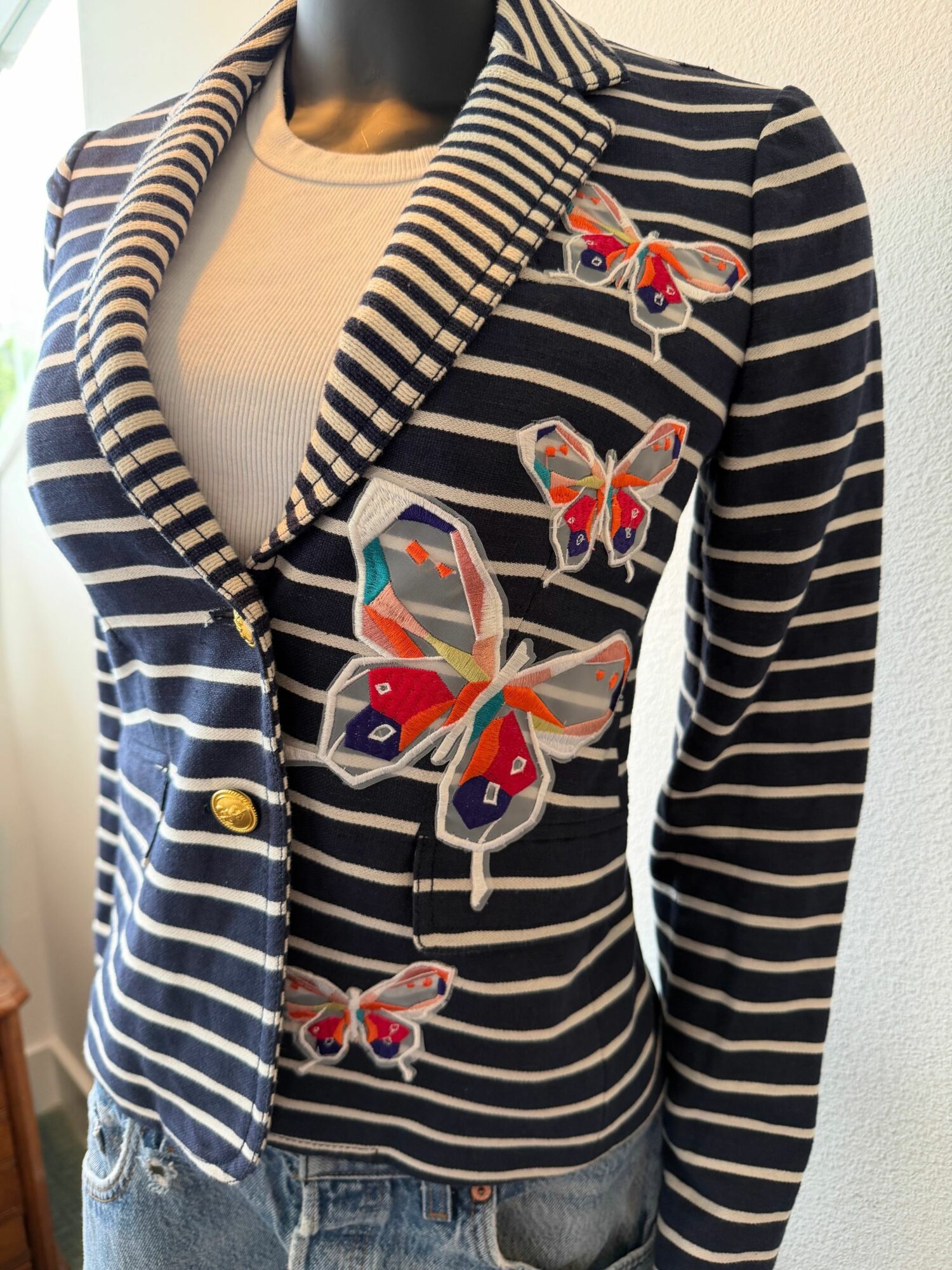 Person wearing a striped jacket with butterfly embroidery, standing sideways, with a white background.