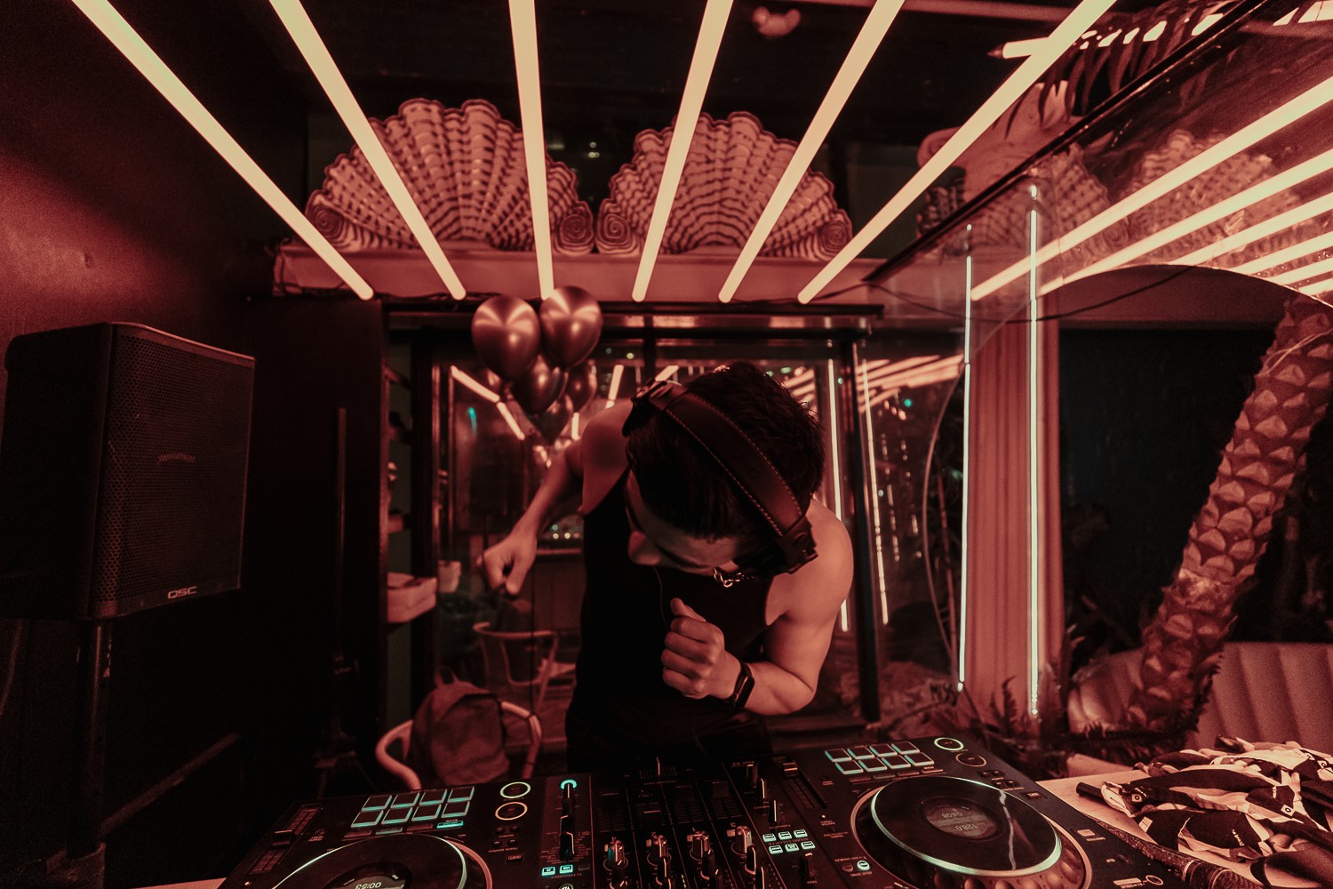Person dancing in a nightclub with colorful lights and reflective surfaces, holding a drink, surrounded by speakers and decorations.