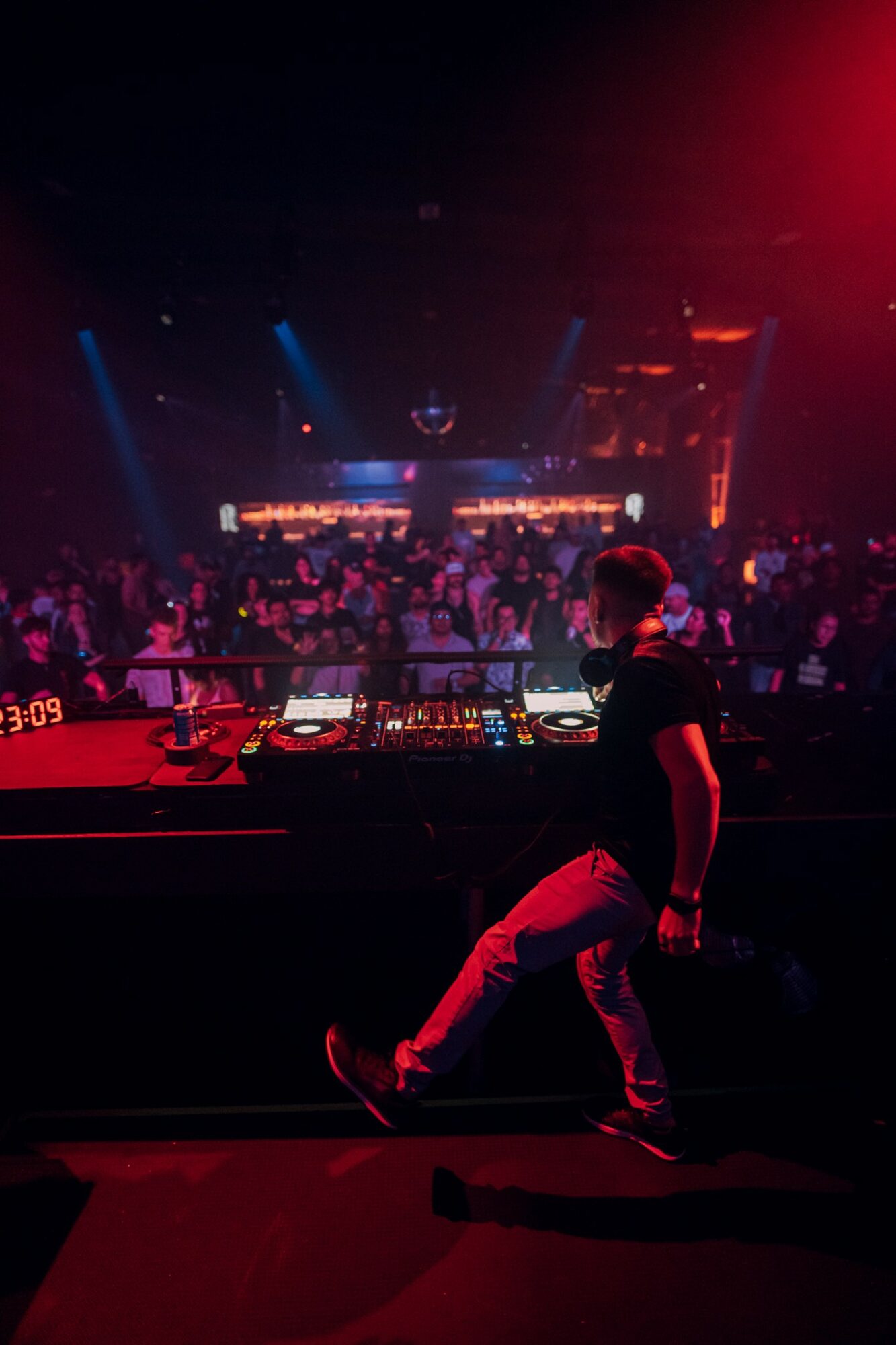 DJ performing on stage with a crowd in a dark, colorful nightclub setting, illuminated by red and blue lights.