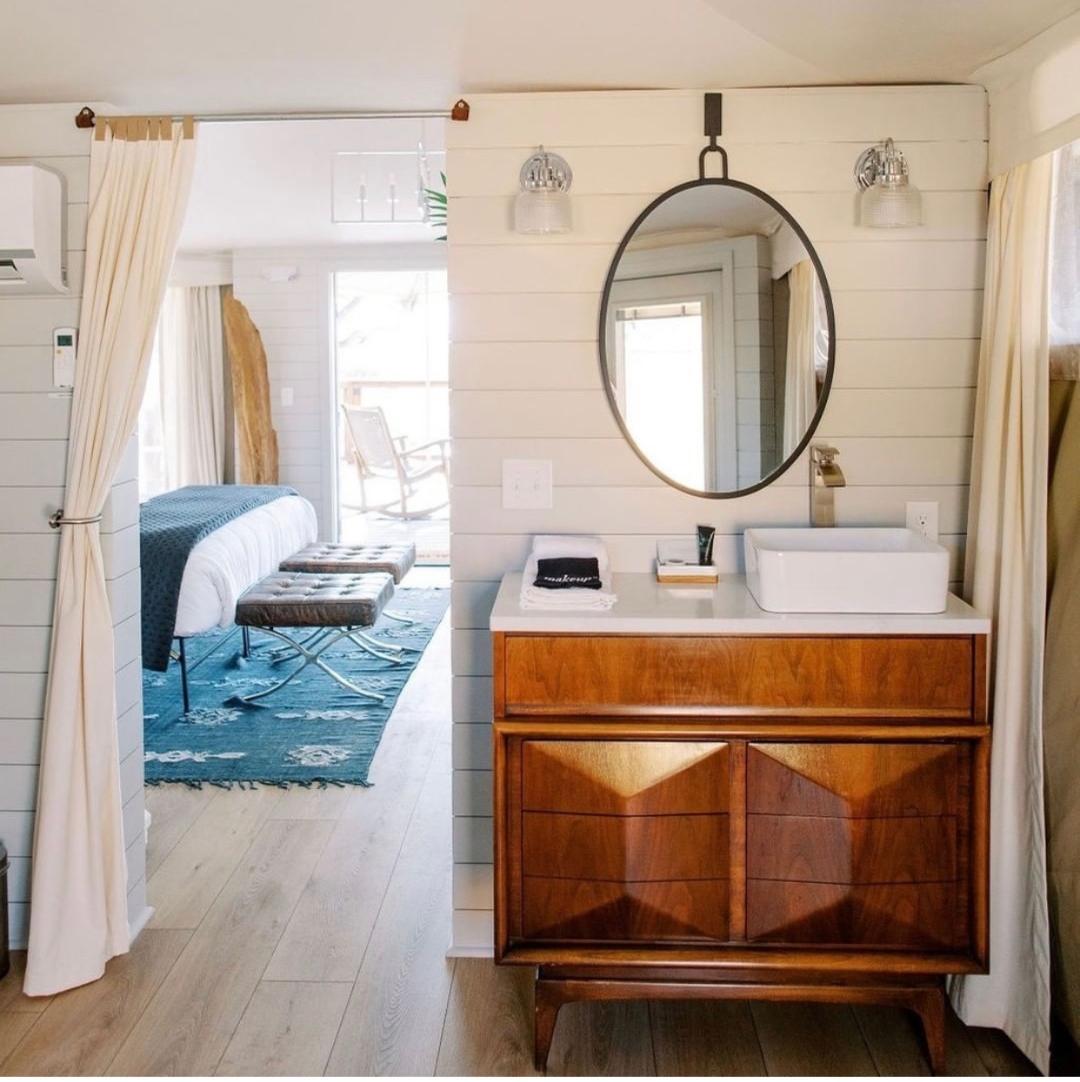 Bathroom vanity with mirror, sink, and wooden cabinet in a bright room with white walls and curtains.